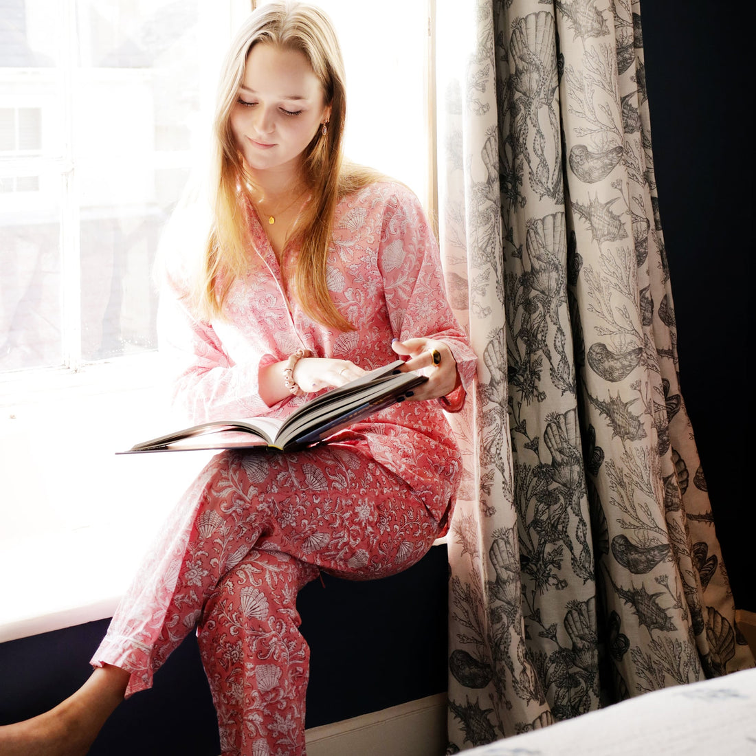 model reading a book in the Jaipur rose pyjamas.