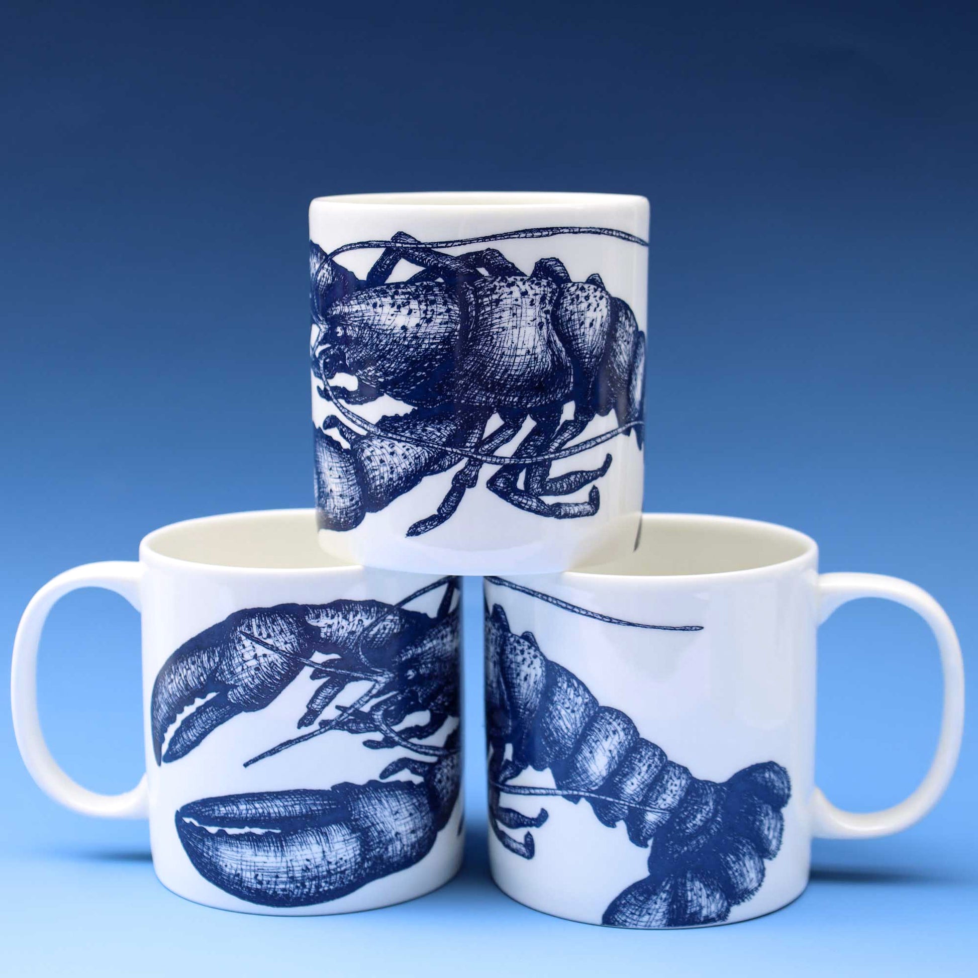 Three white ceramic mugs with dark blue lobster illustrations, arranged in a pyramid-like stack against a blue gradient background.