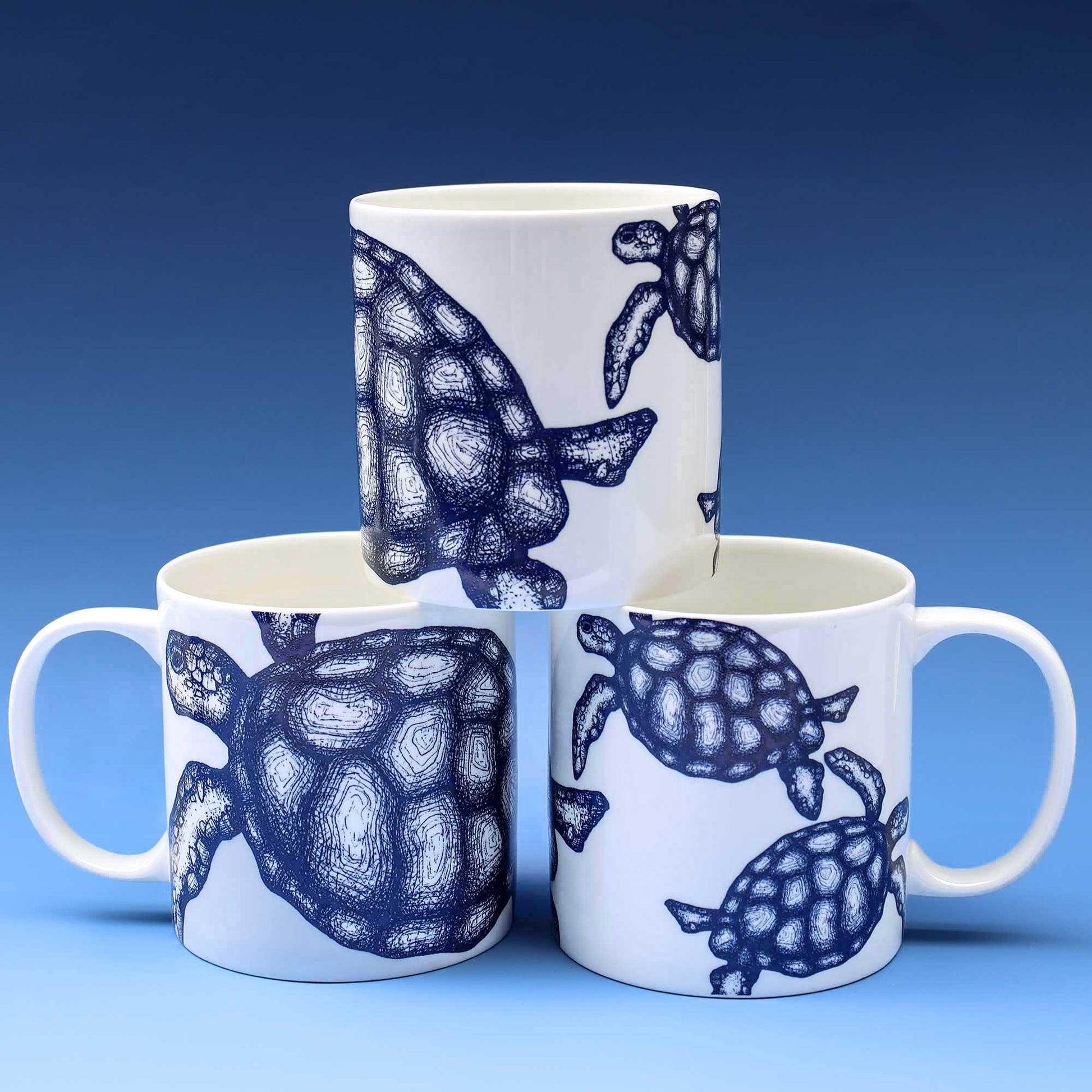 Stack of 3 white mugs with navy turtle illustrations and showing different sides , all on a graduated blue background.