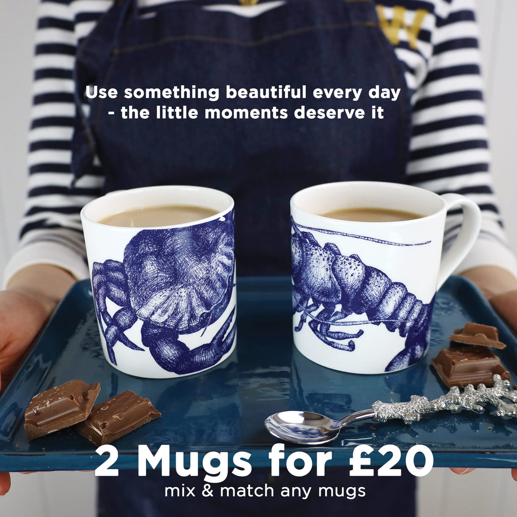 Cream Cornwall sea life mugs with crab and lobster illustrations filled with coffee, served on a tray with chocolate, promoting the 2 mugs for £20 mix and match offer.