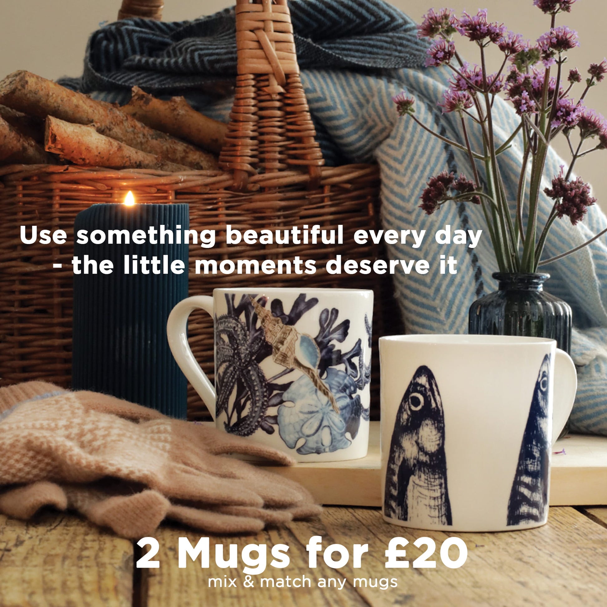 Two Cream Cornwall ceramic mugs with mackerel heads and beachcomber designs styled with flowers, gloves and candle on a rustic table, promoting the 2 mugs for £20 offer.