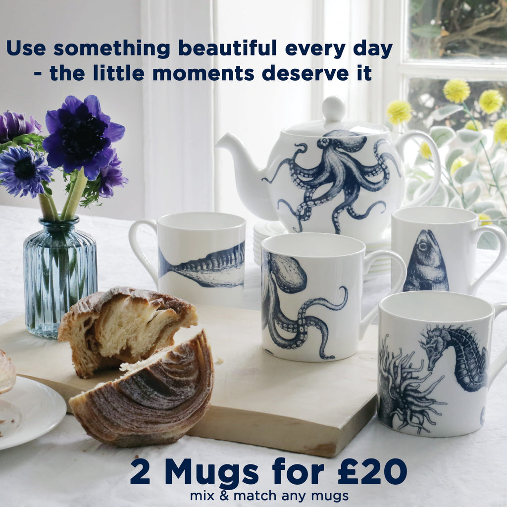 Cream Cornwall sea life ceramic mugs with octopus, fish and seahorse illustrations styled with pastries and flowers on a breakfast table, mix and match mugs 2 for £20.