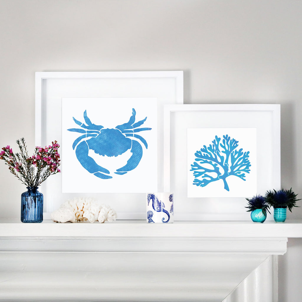 A coastal-themed mantelpiece display featuring two framed blue illustrations—one of a crab and the other of coral—both in white mounts. The arrangement is complemented by decorative elements including a navy blue glass vase with pink flowers, white coral pieces, a blue and white ceramic cup with a seahorse design, and small turquoise vases with spiky blue flowers.



A coastal-themed mantelpiece display featuring two framed blue illustrations—one of a crab and the other of coral—both in white mounts. Th


