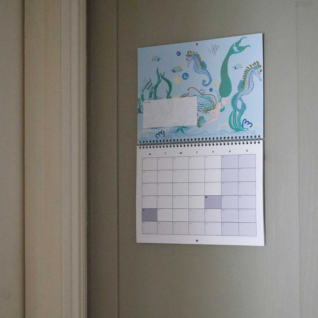 Cream Cornwall 2027 wall calendar open to March, featuring a colourful mermaid, seahorses and marine life illustration with a month-to-view planner and notes section.