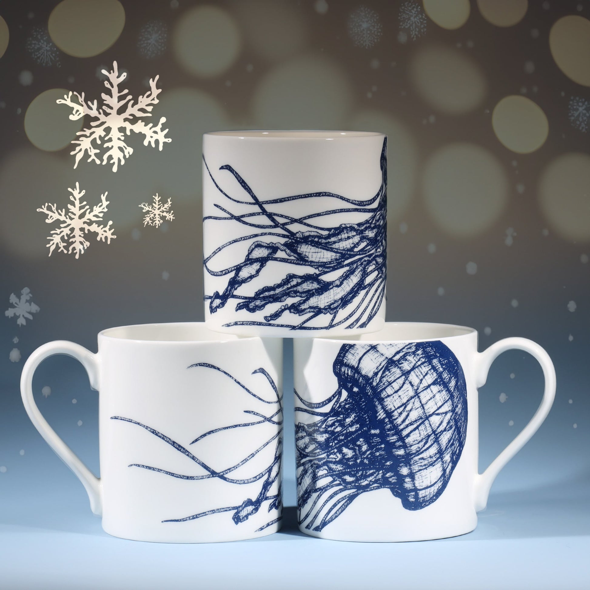 Three white mugs featuring intricate blue jellyfish illustrations arranged in a pyramid shape, set against a softly lit festive background with delicate snowflakes and small, warm golden lights.