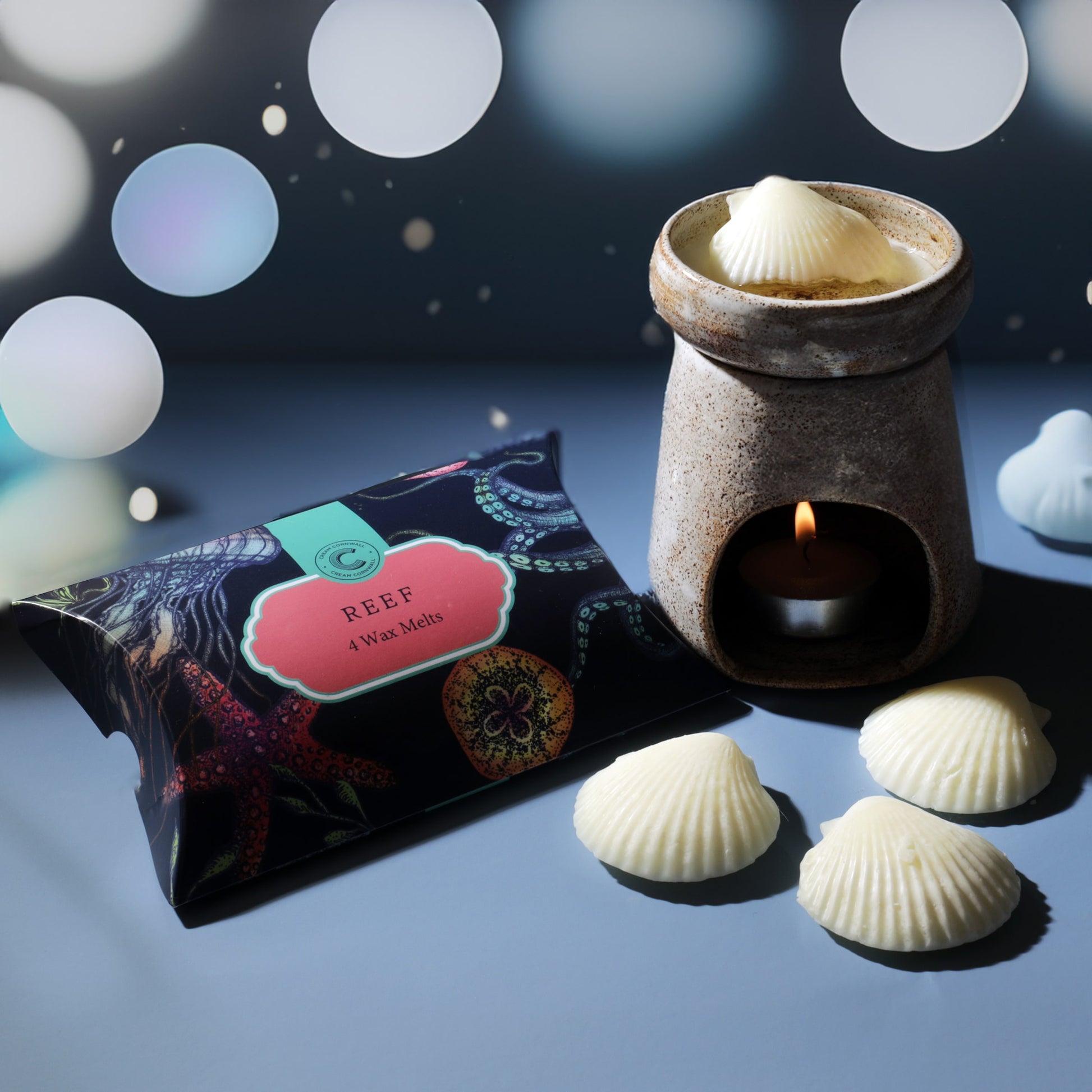 Candle warmer with shell-shaped candles and a box labeled 'Reef' on a blurred background