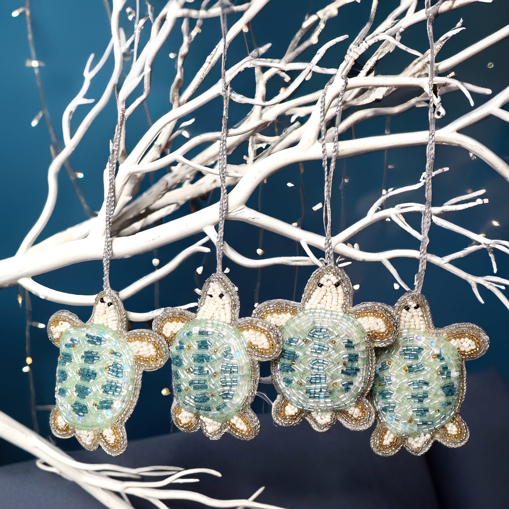 Four beaded turtle ornaments hanging on a branch against a dark background