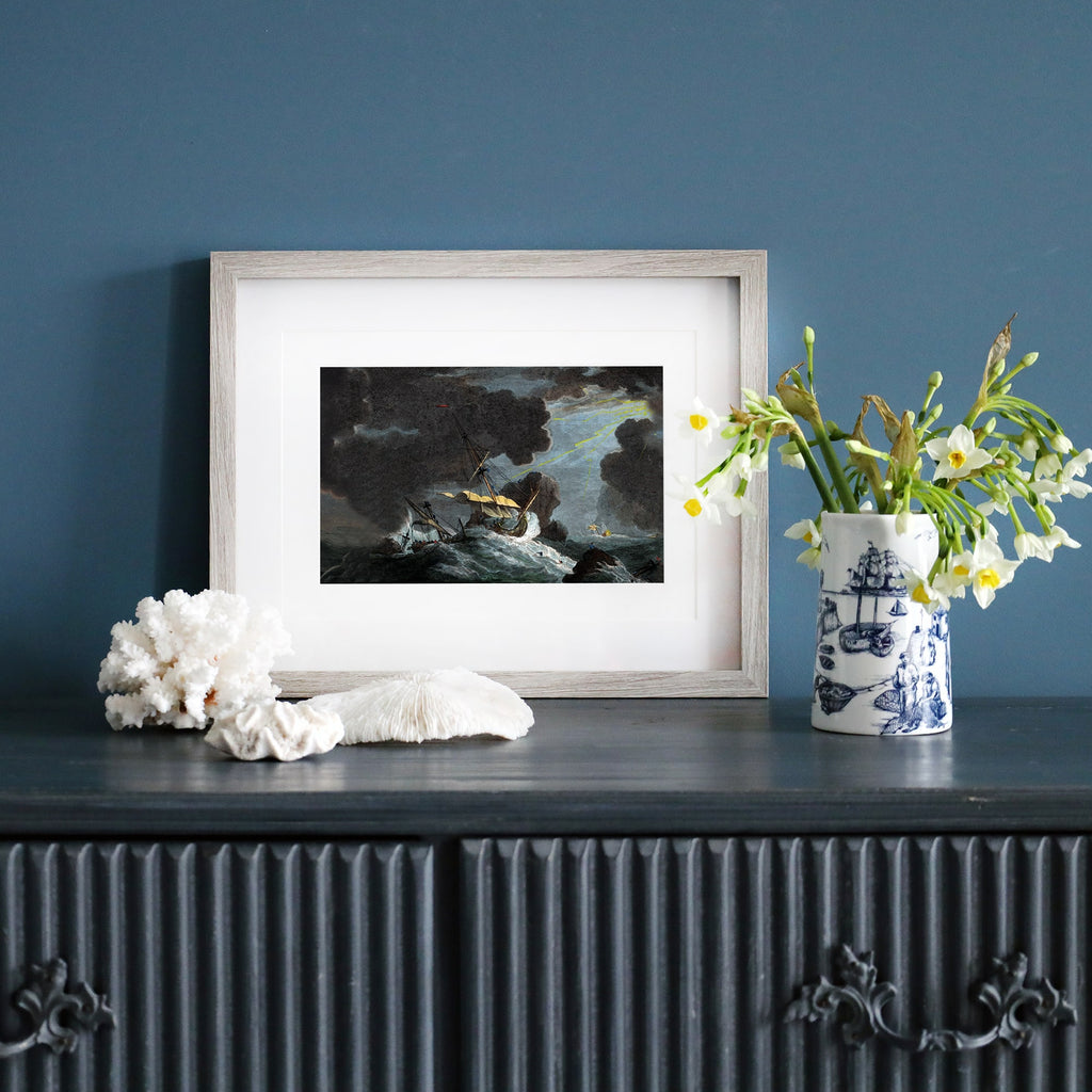 Framed print of a stormy shipwreck scene with towering waves, dark clouds, and a dramatic beam of light breaking through.