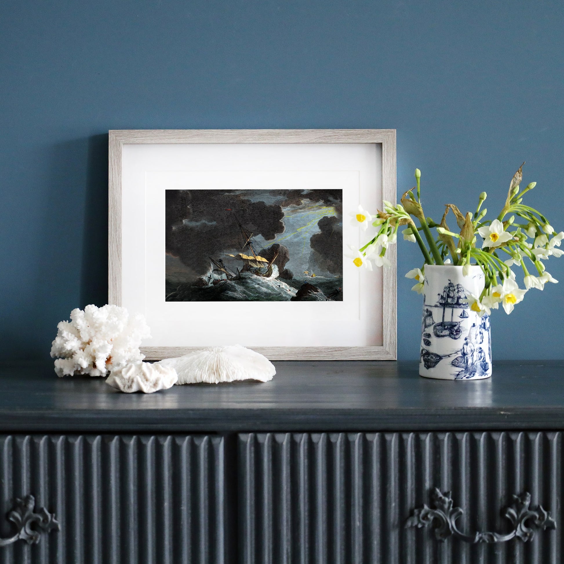 Framed print of a stormy shipwreck scene with towering waves, dark clouds, and a dramatic beam of light breaking through.