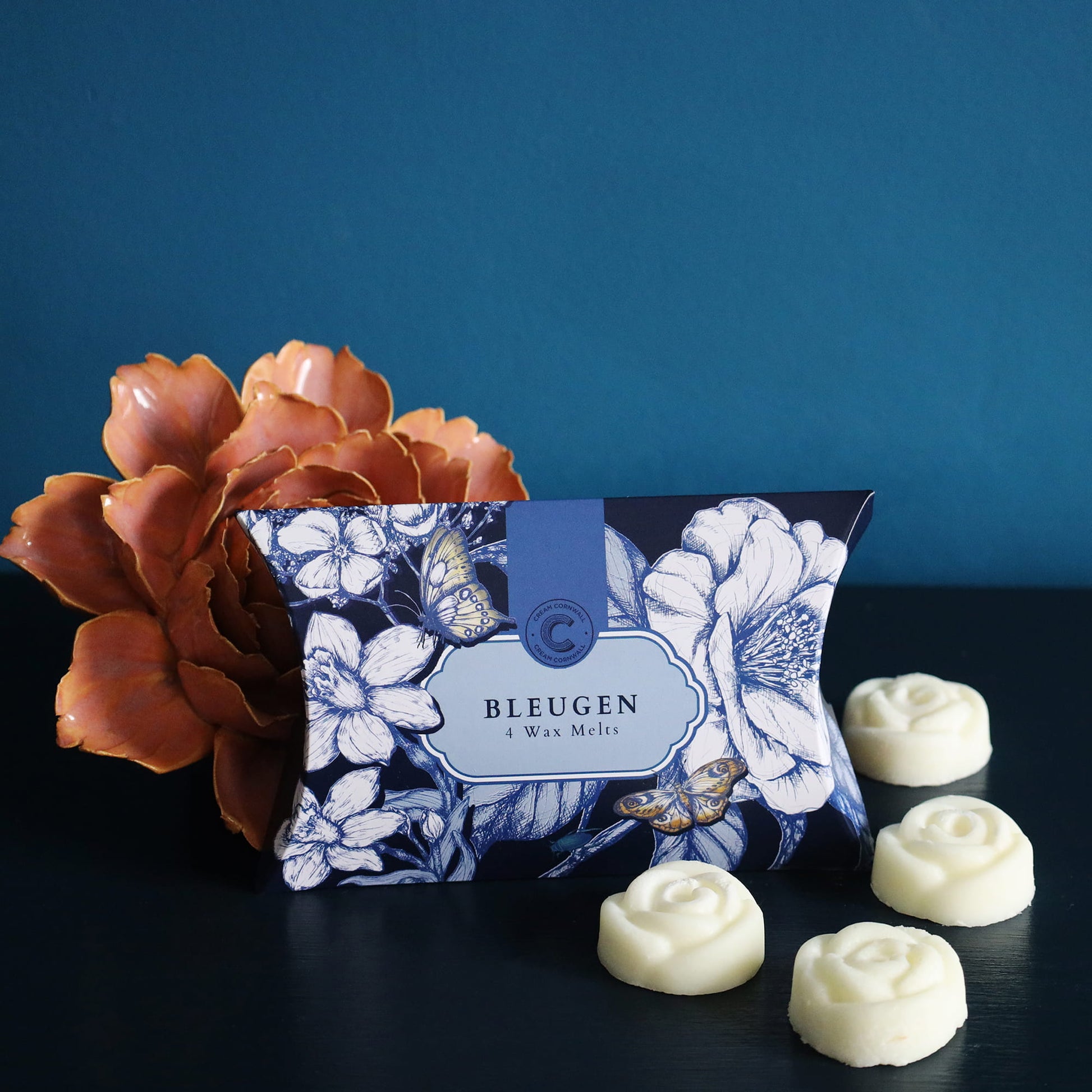 Floral packaging of BLEUGEN with white wax melts on a dark surface against a blue background