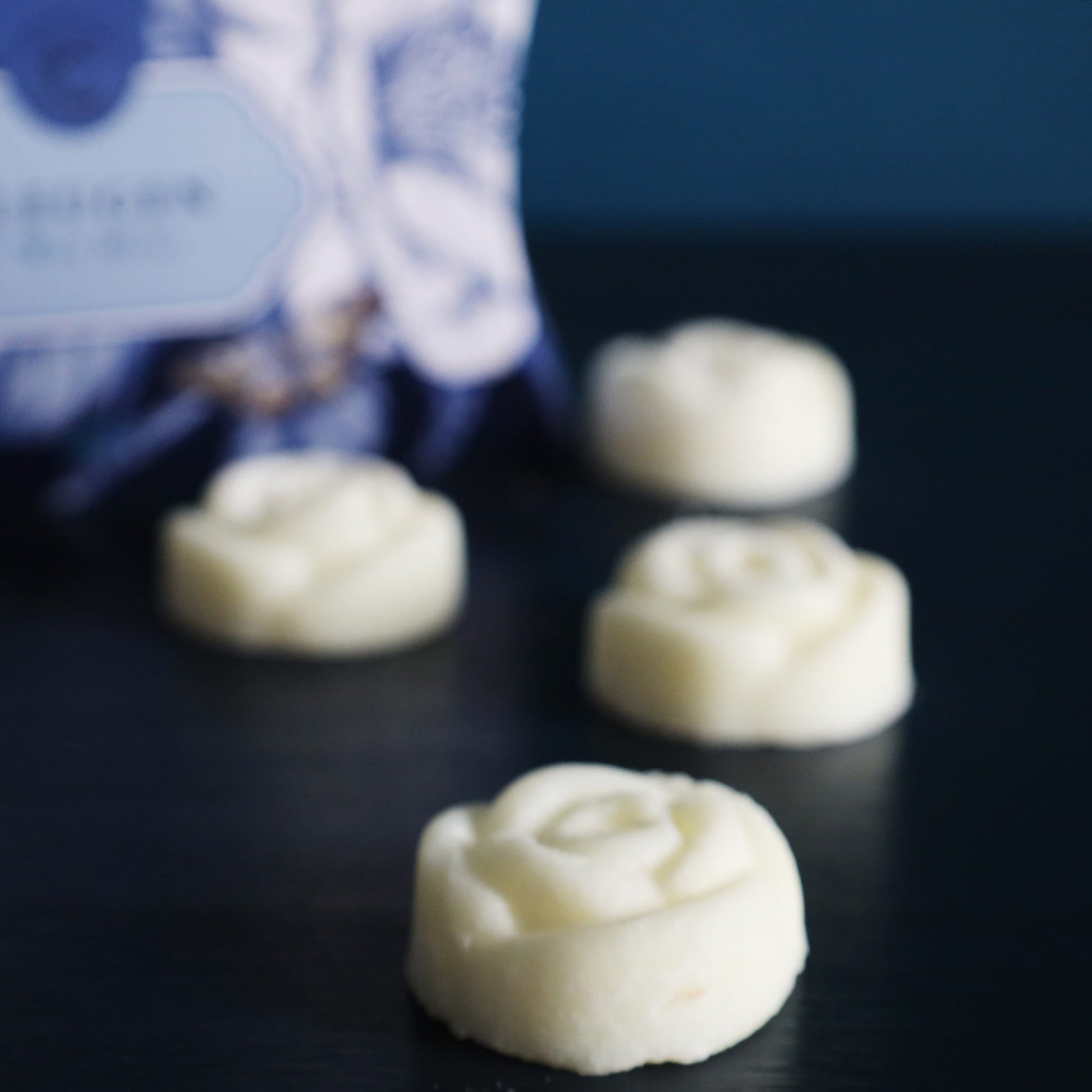 White rose-shaped cookies on a dark surface with a blurred blue box in the background.