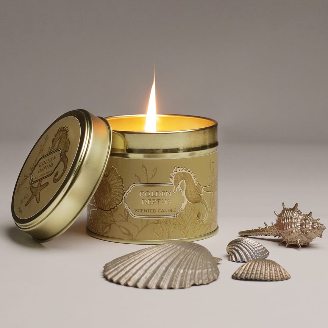 Gold candle in a decorative tin with seashells on a neutral background