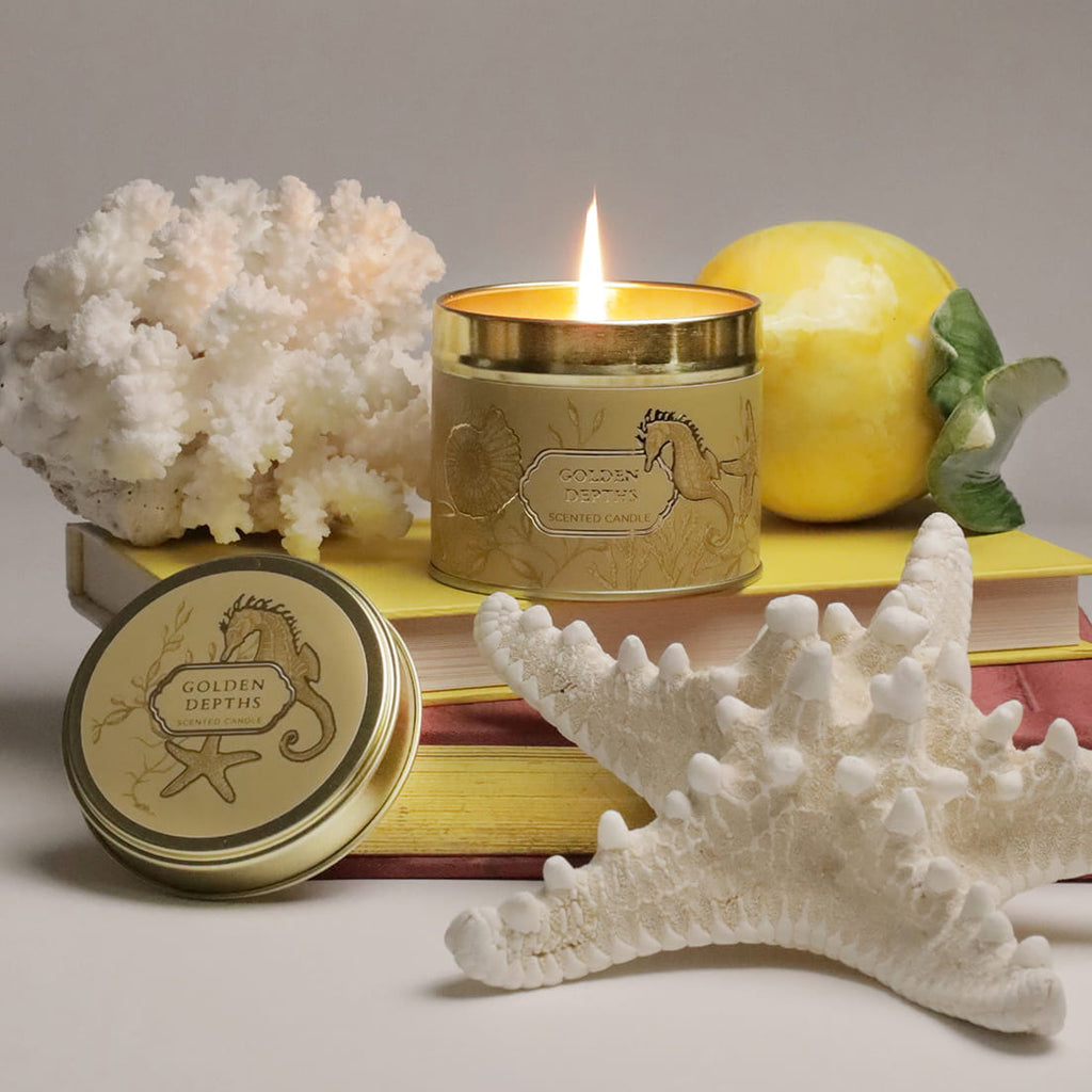 Candle with 'Golden Depths' branding on a decorative surface with coral and lemon.