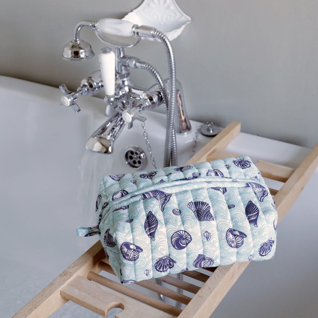Patterned toiletry bag on a bath caddy next to a bathtub with shower head and faucet.