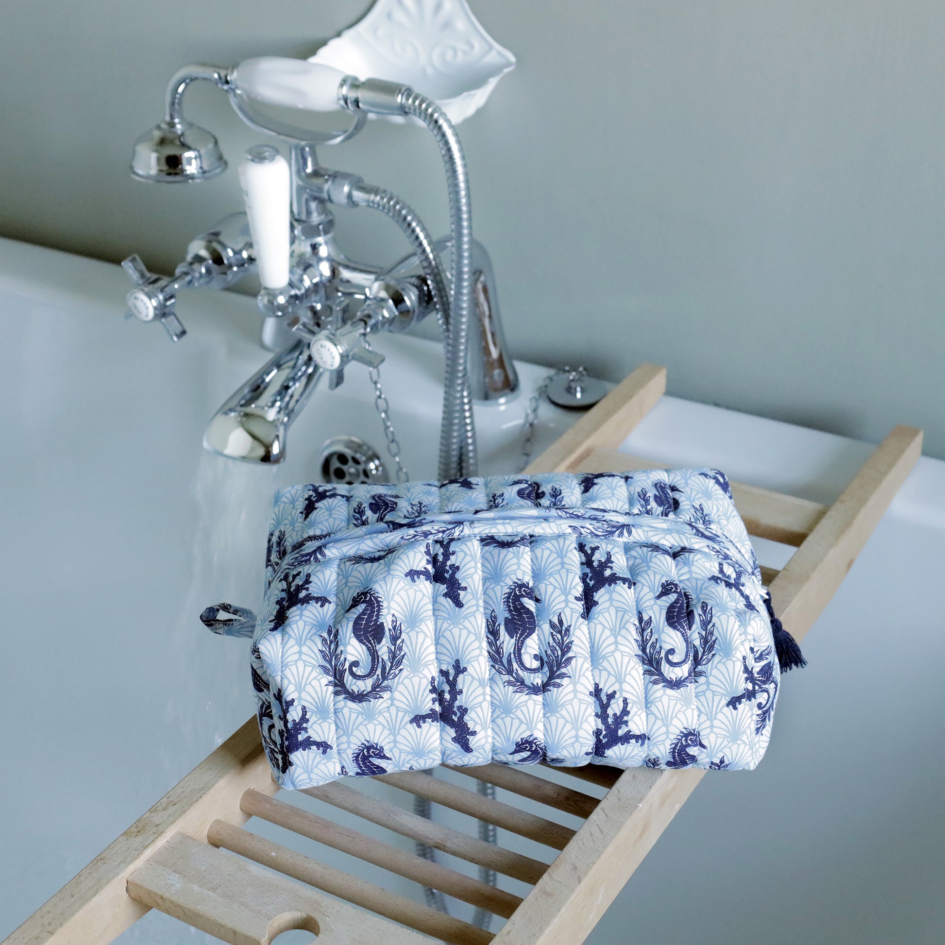 Blue and white patterned toiletry bag on a wooden stand with a bathtub in the background