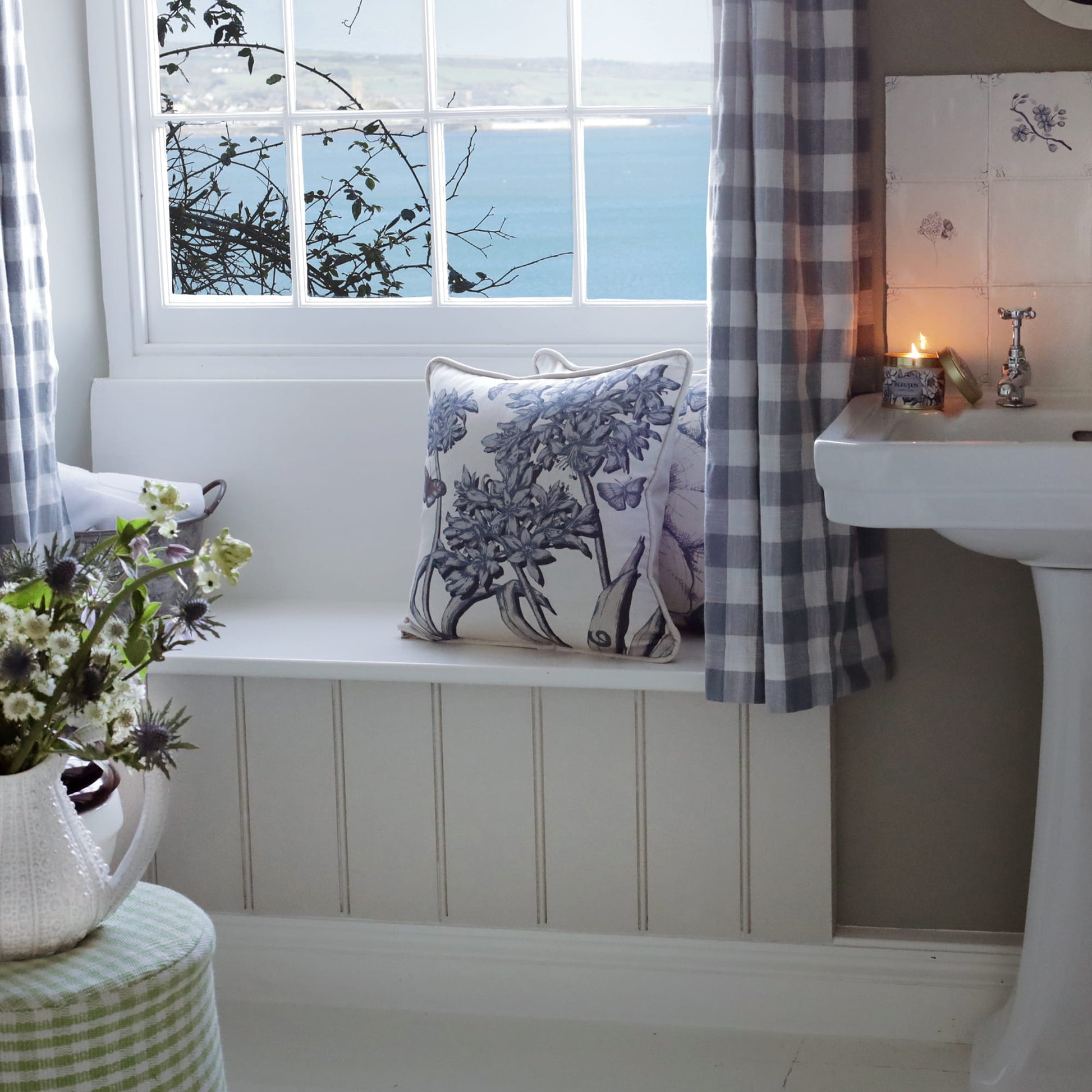Bathroom with a window, sink, and decorative agapanthus pillow on a bench.
