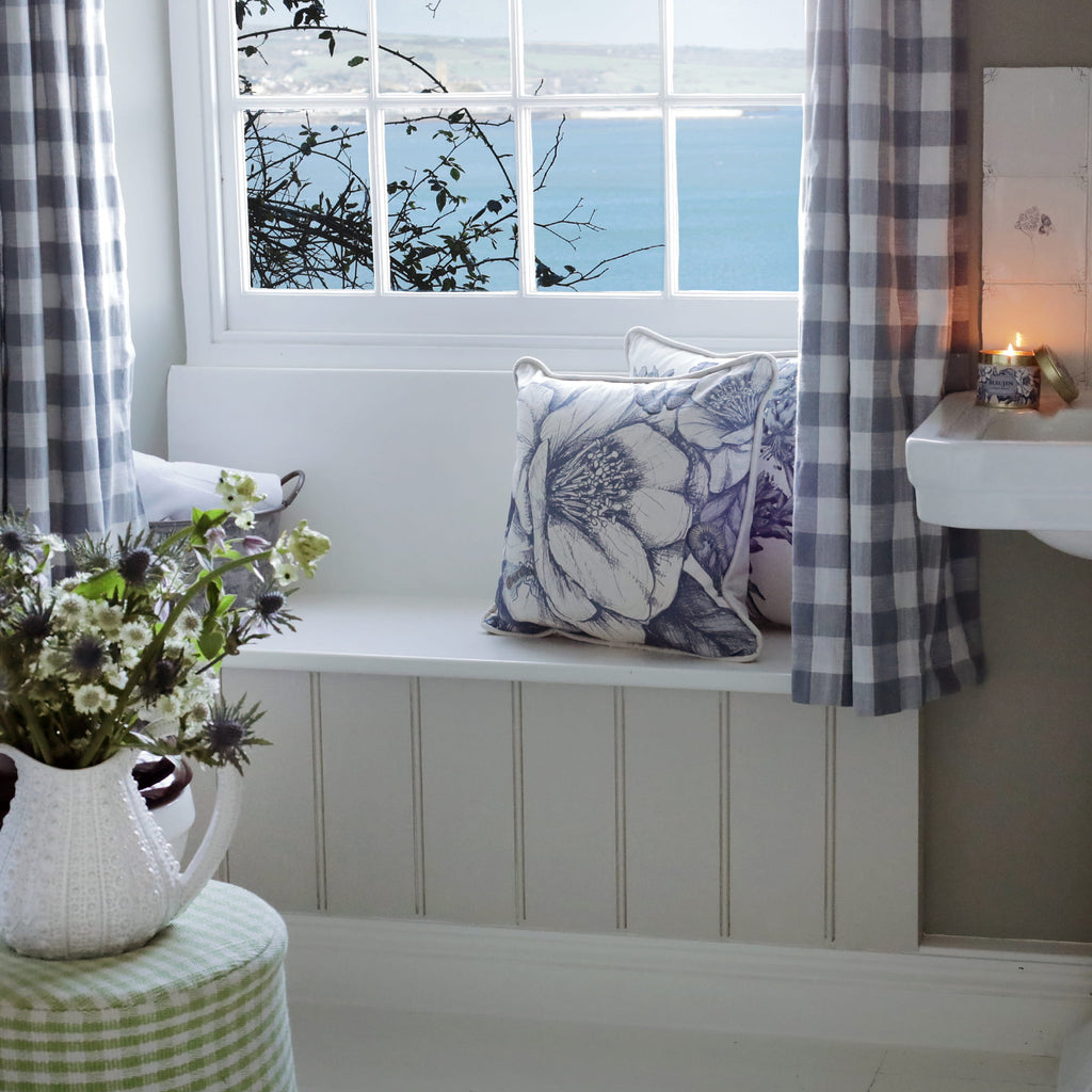 Nautical-themed room with checkered curtains, camelia floral pillows, and a window view of the sea.