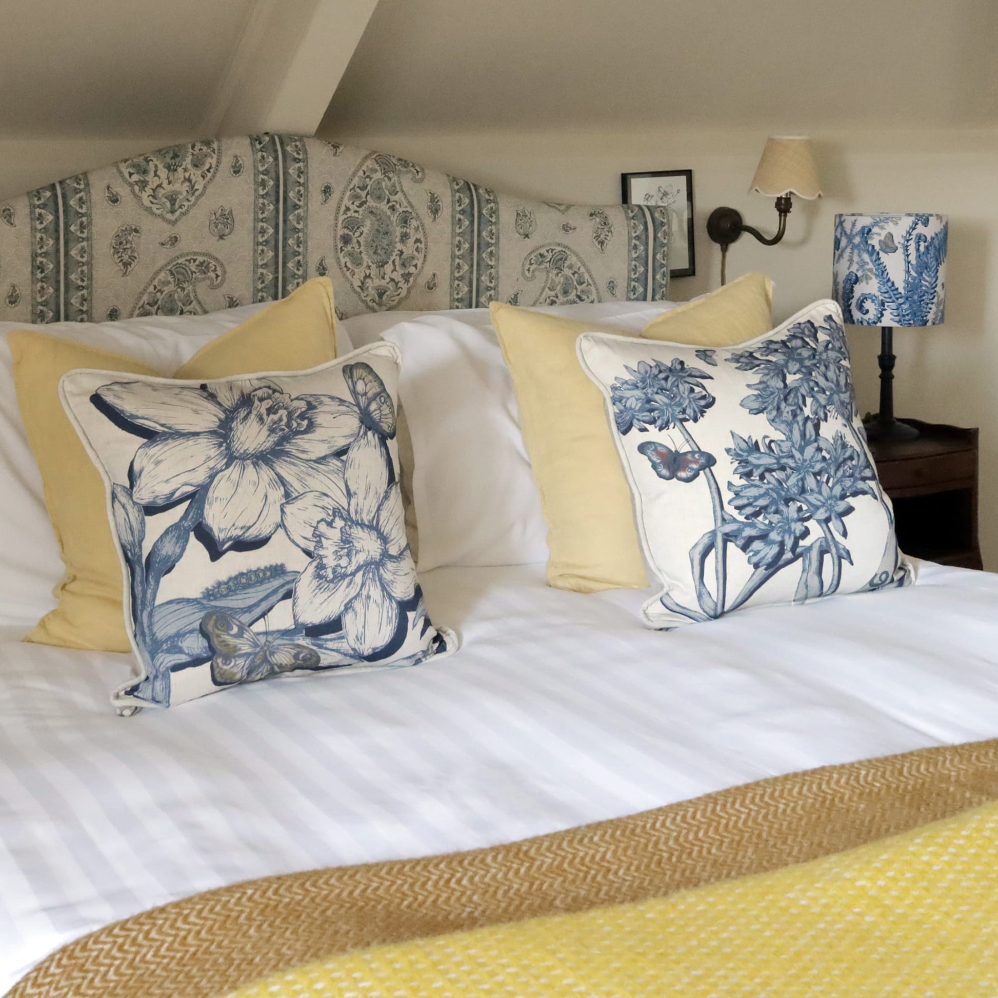 Decorative pillows with daffodil & agapanthus patterns on a bed in a bedroom setting.