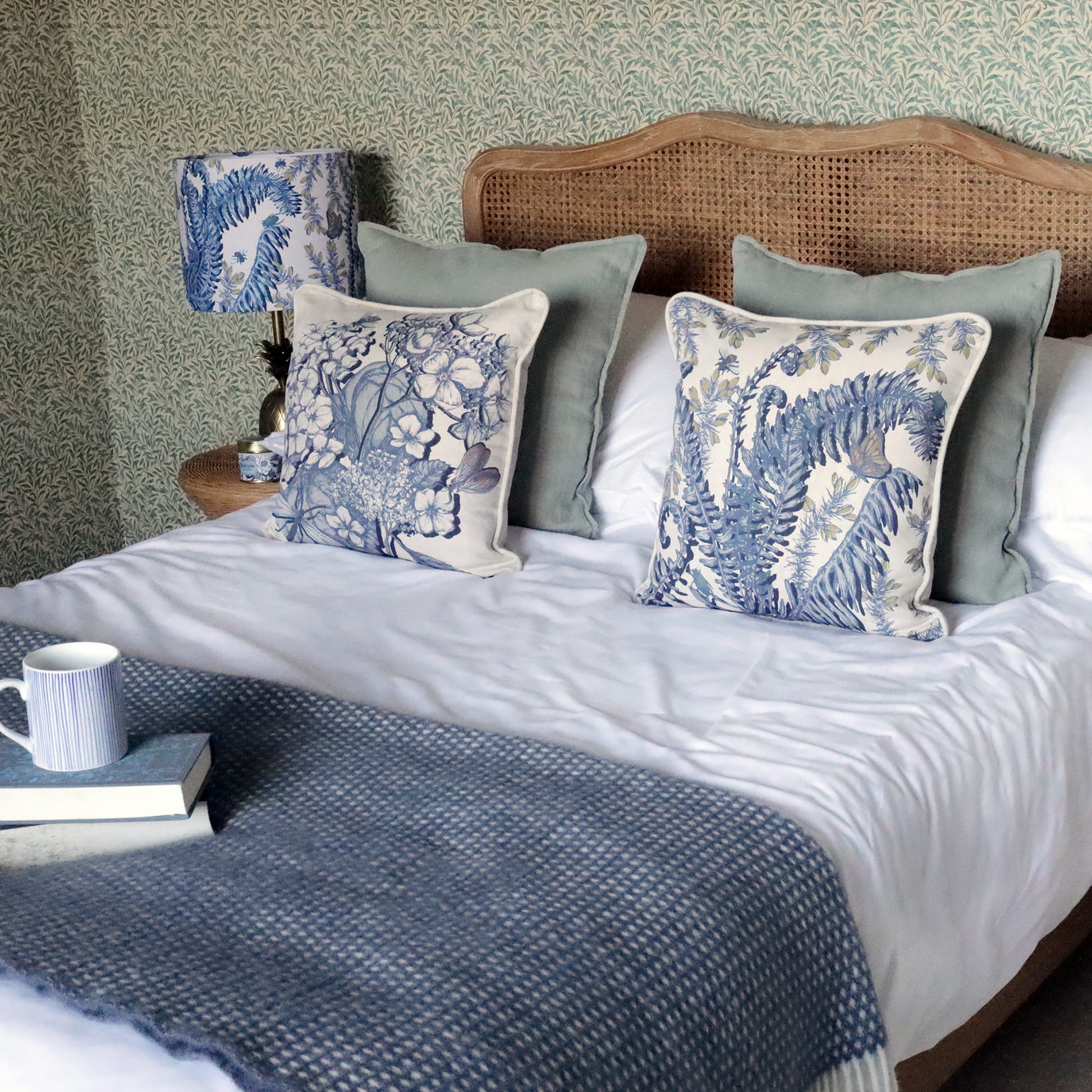 Bedroom with a bed featuring blue fern & hydrangea patterned pillows and a wooden headboard.