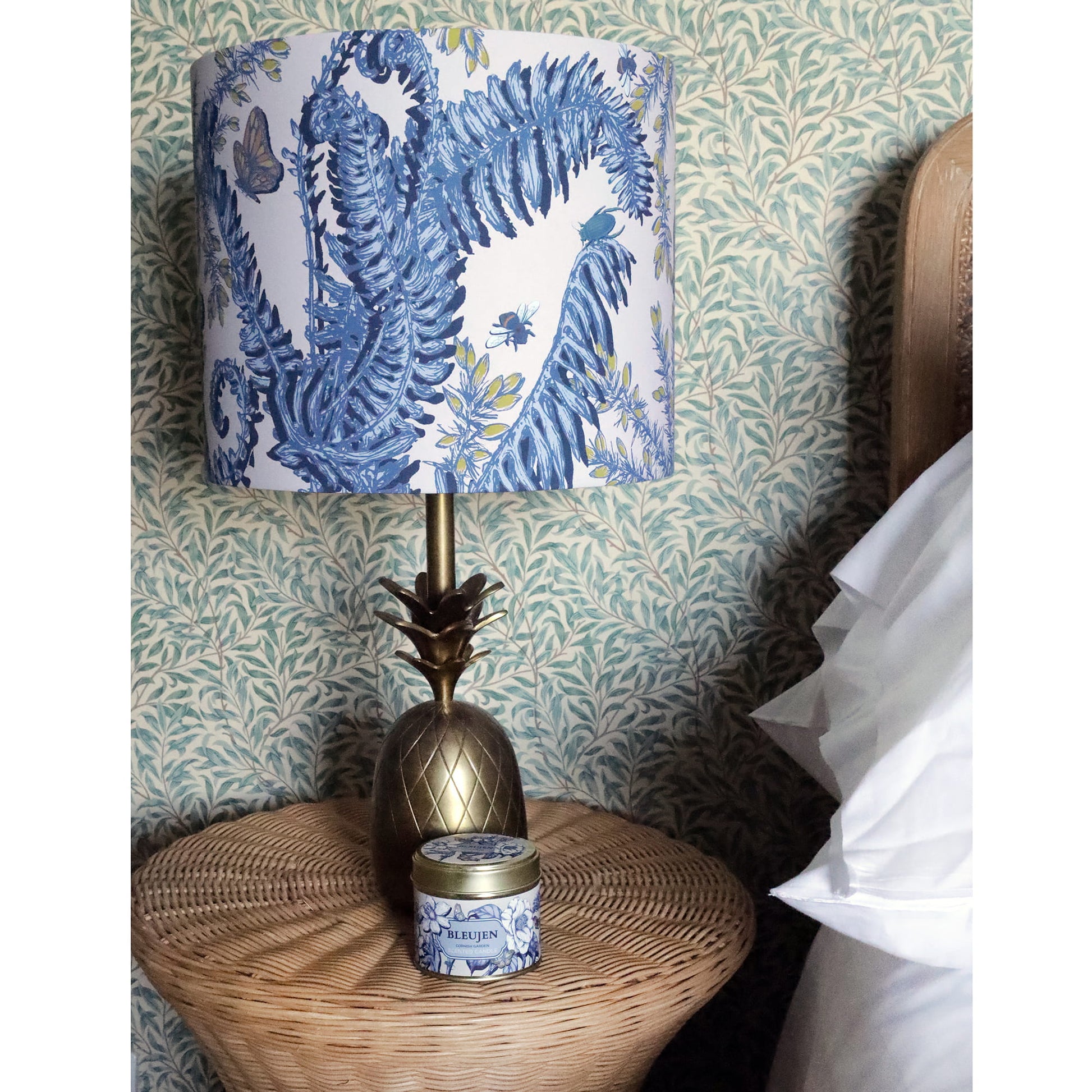 Decorative lamp with blue floral fern & gorse patterned shade on a bedside table.