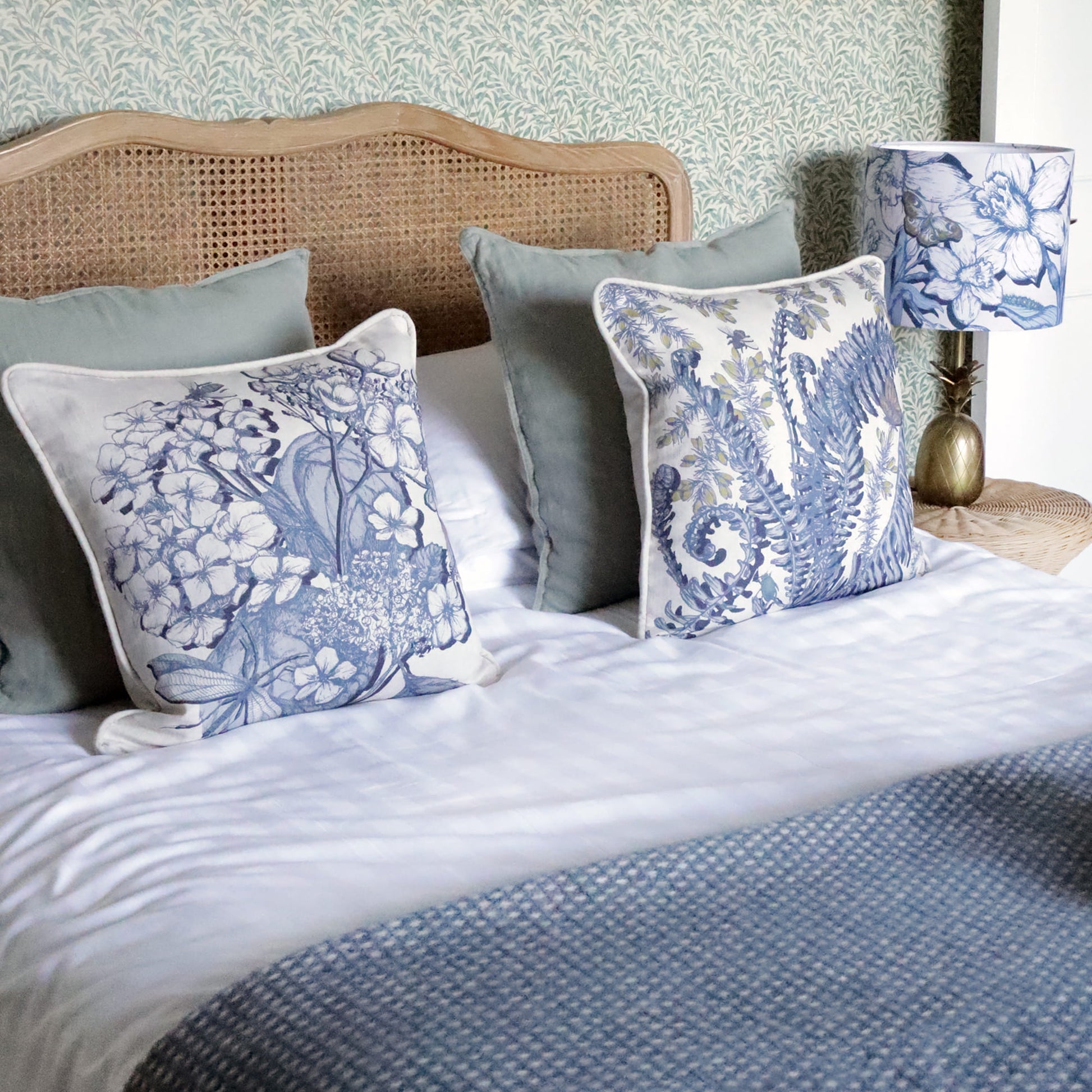 Bed with decorative hydrangea & fern pillows and a lamp in a bedroom setting.