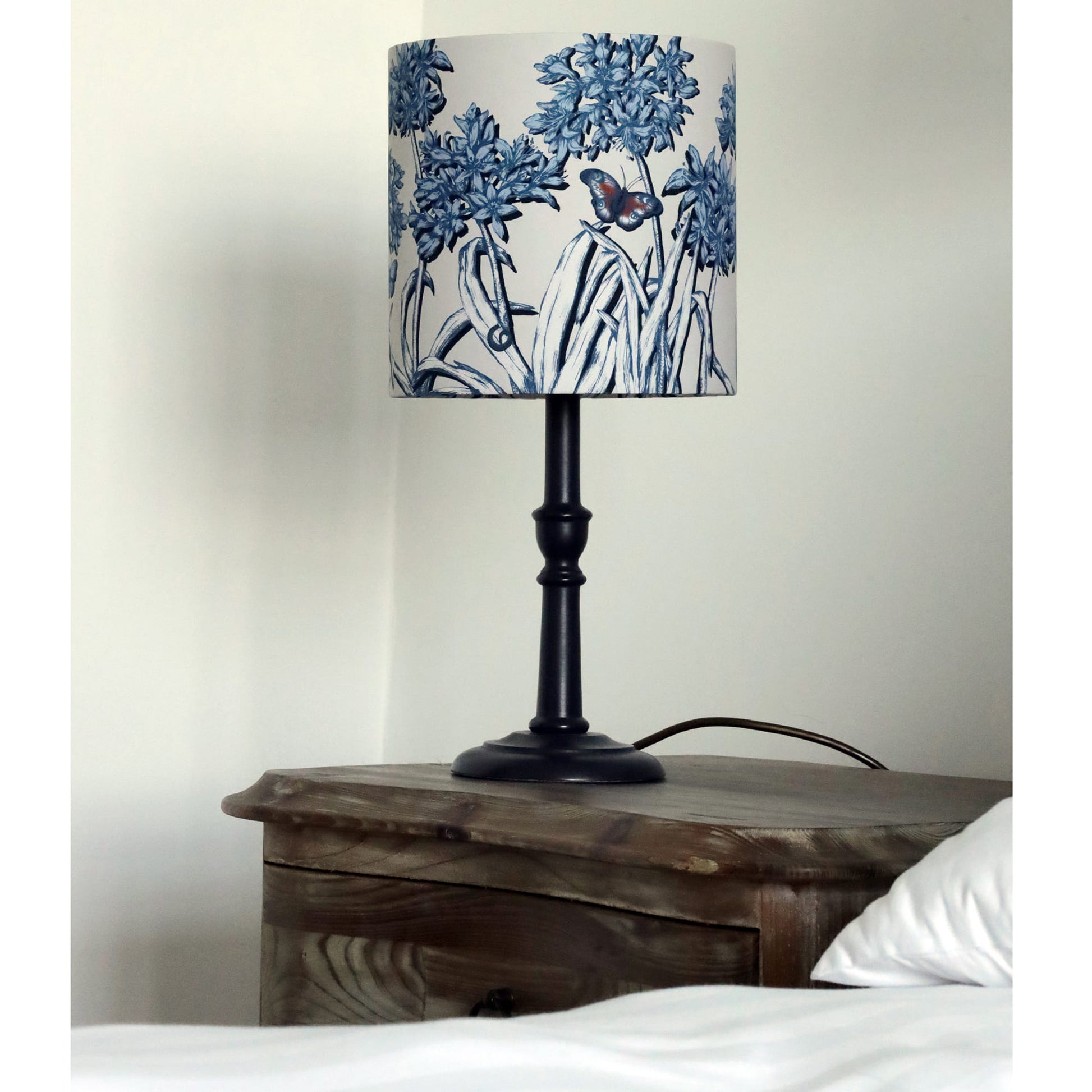 Table lamp with agapanthus patterned shade on a wooden nightstand.