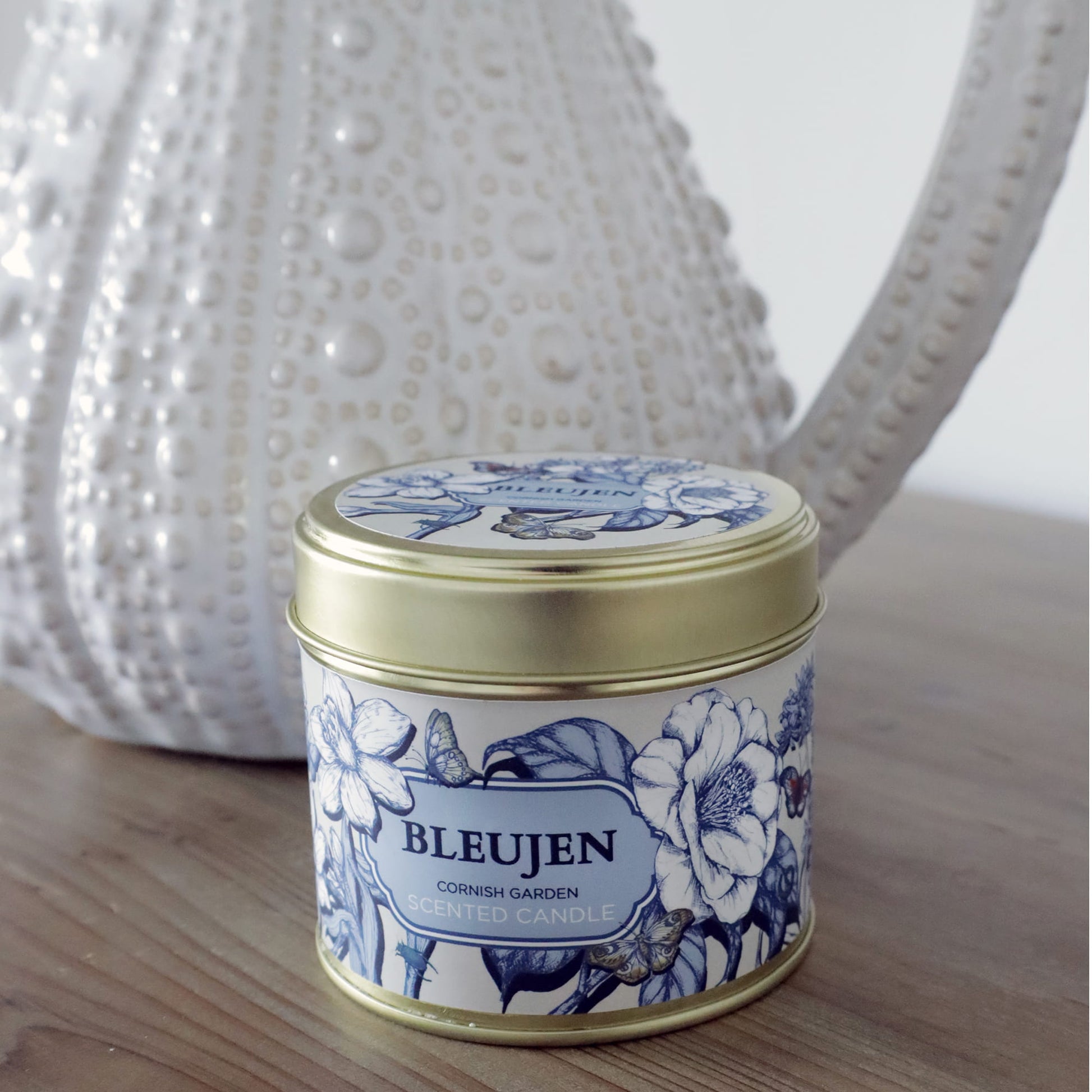 Bleujen candle in a decorative tin with floral design on a wooden surface.