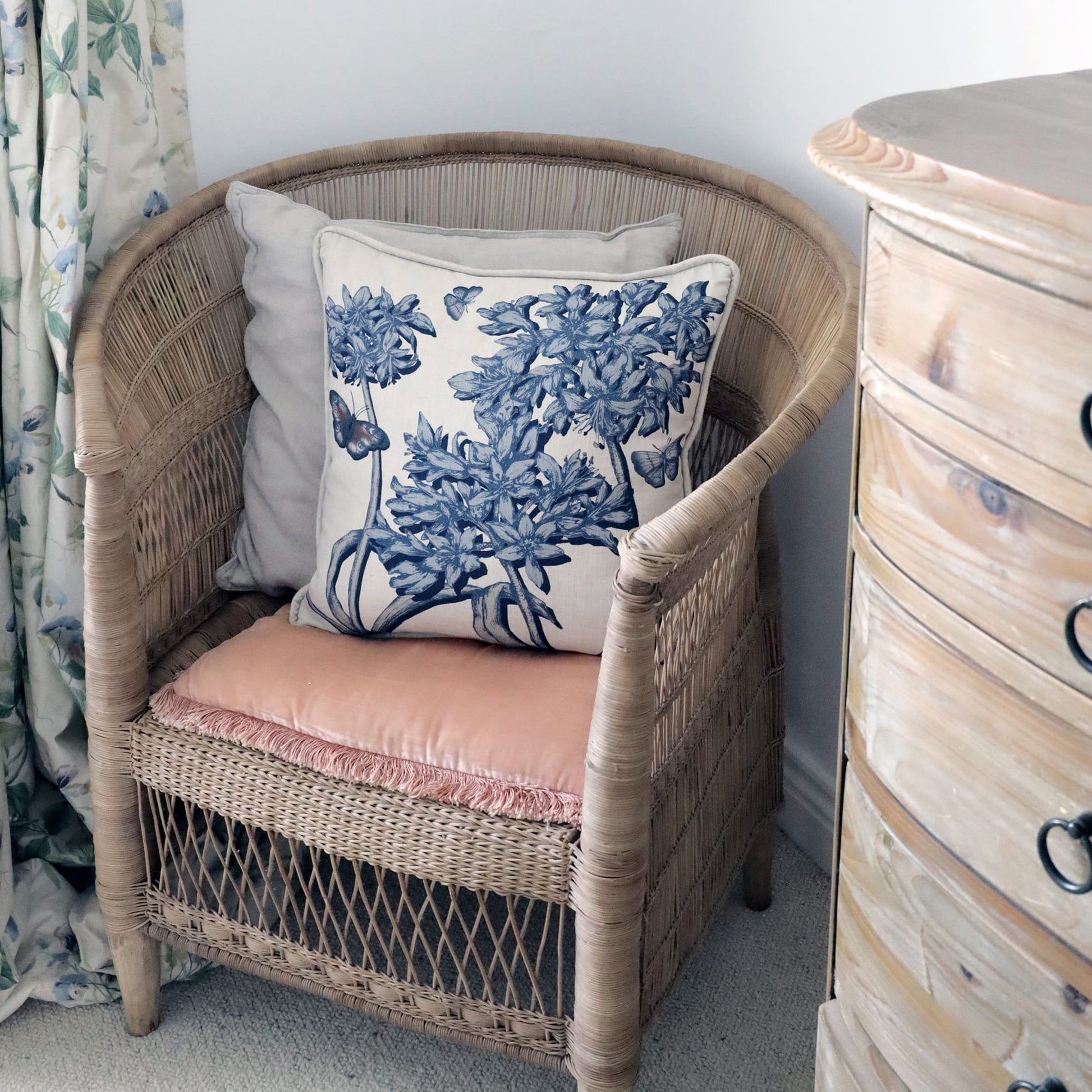 Wicker chair with agapanthus floral pillow next to a wooden dresser