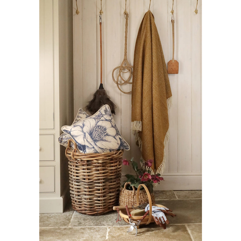 Wicker basket with decorative pillow, blanket, and small plant against a wooden wall.