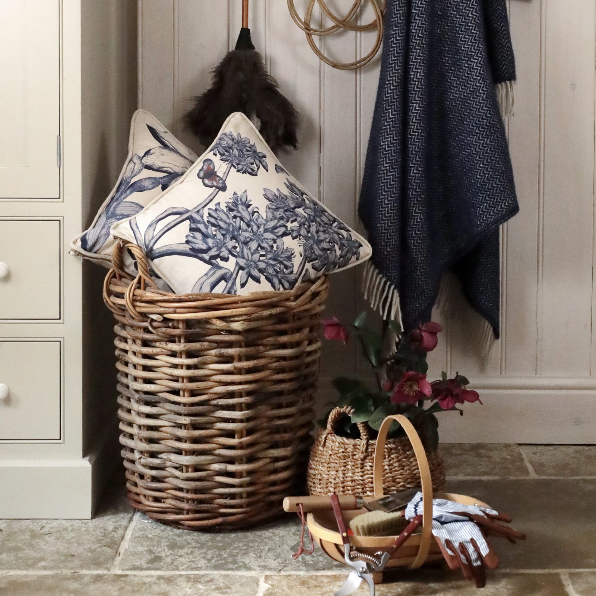 Wicker basket with decorative pillows and a plant in a room setting.