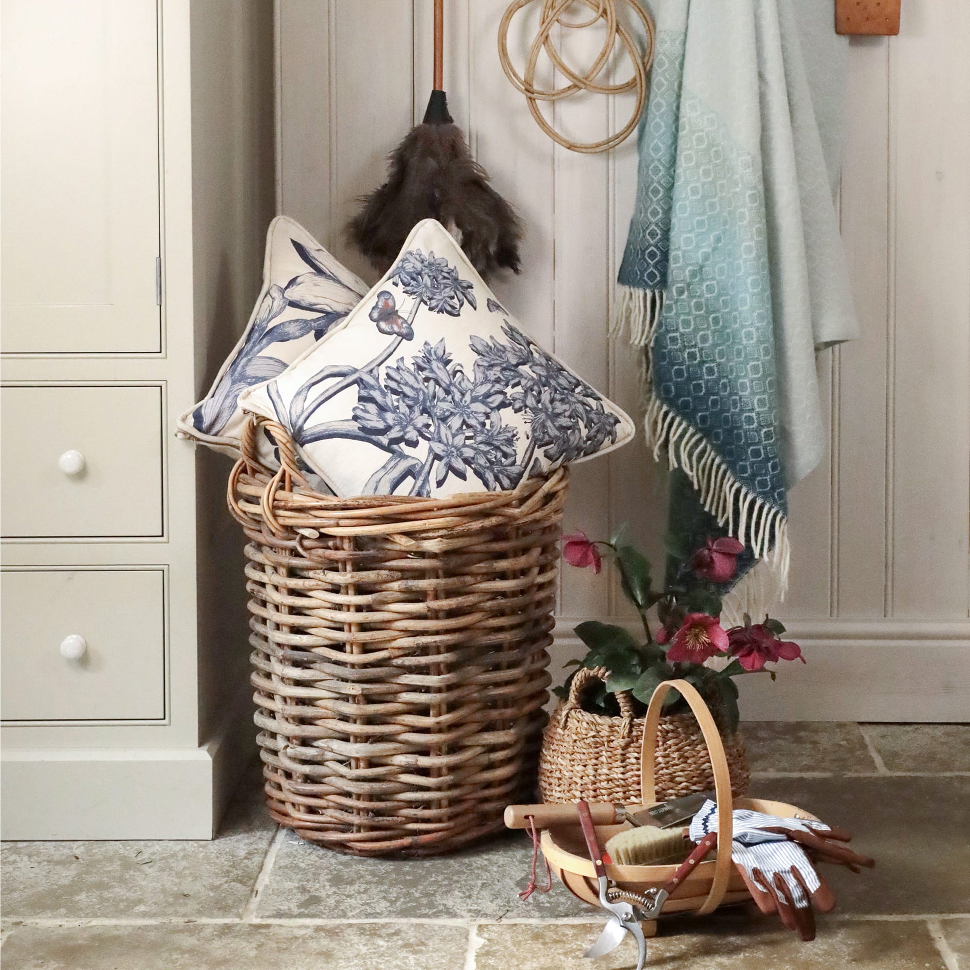 Wicker laundry basket with decorative pillows and a towel in a home setting.