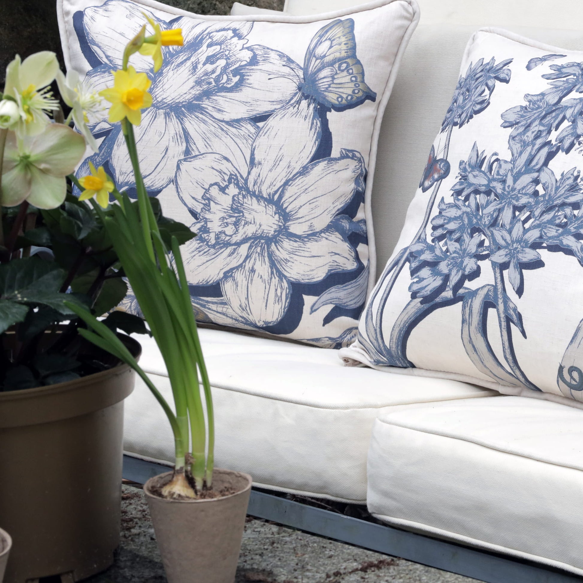 White sofa with daffodil floral-patterned cushions and potted plants.