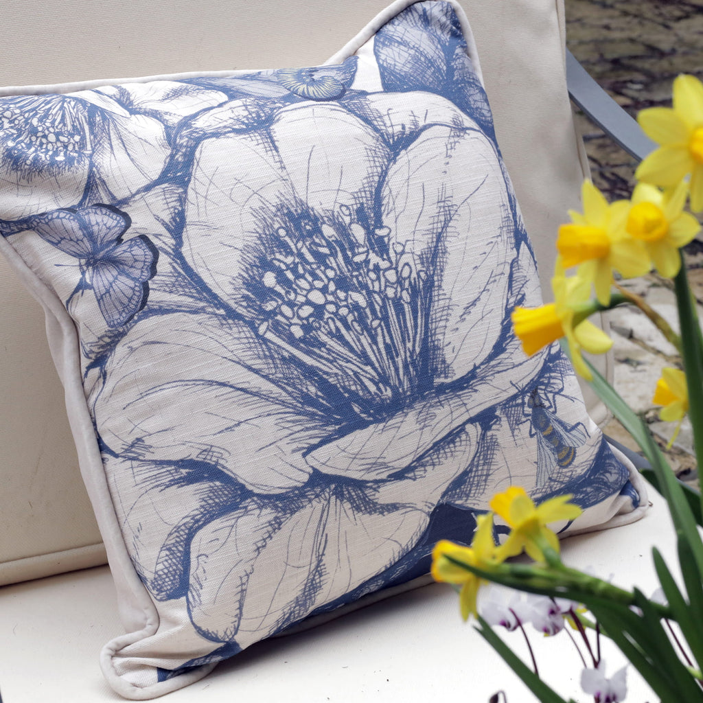 Camelia patterned pillow with blue flowers and white background, accompanied by yellow daffodils.