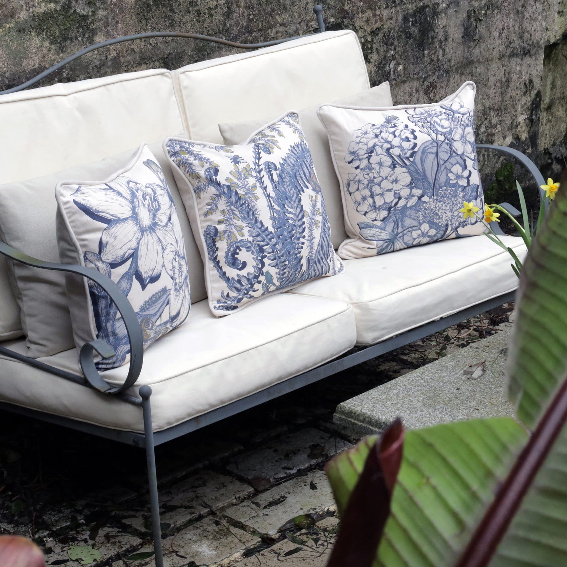 White outdoor sofa with blue floral cushions against a stone wall.
