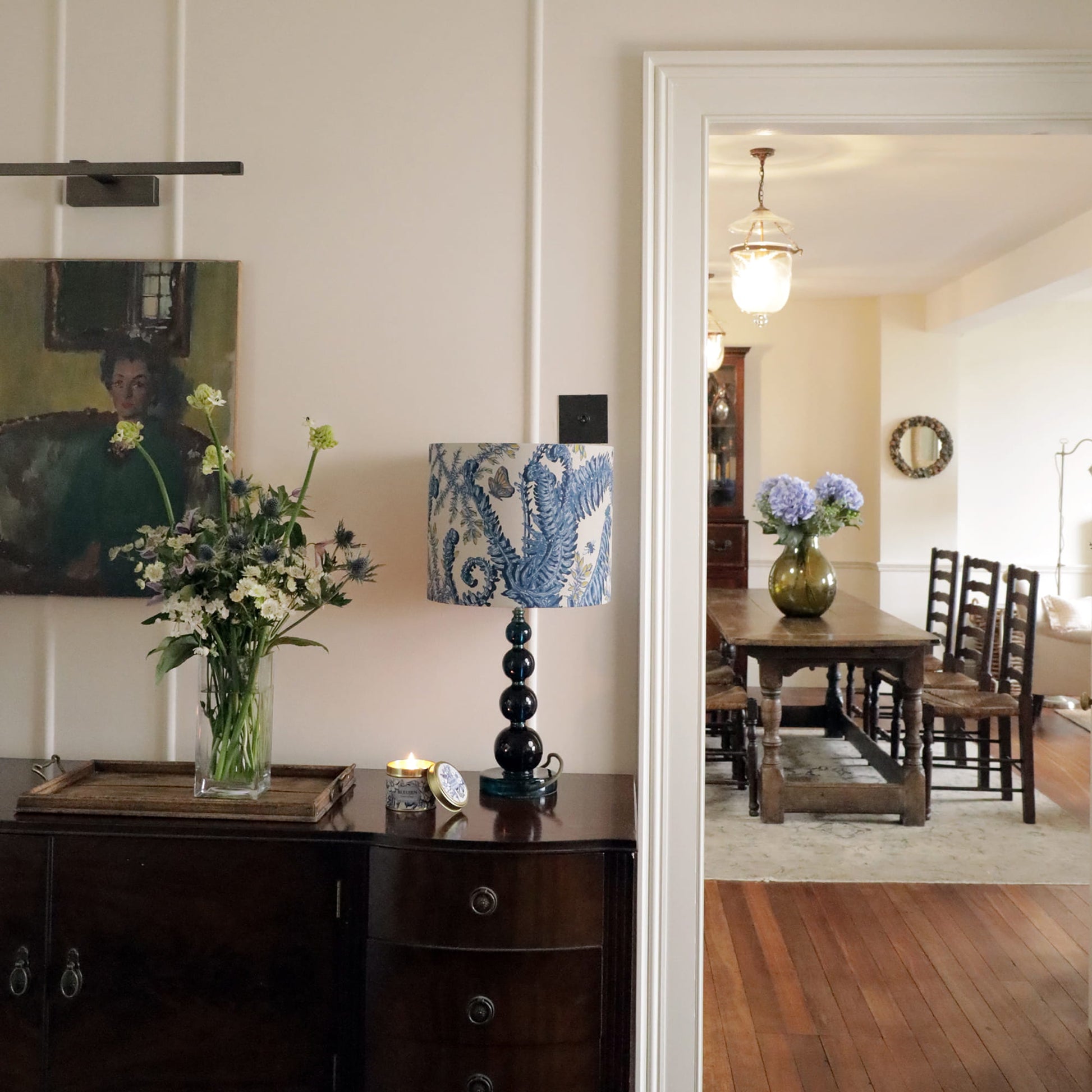 Dining room with a fern & gorse lampshade, flowers, and a mirror reflecting another part of the room.