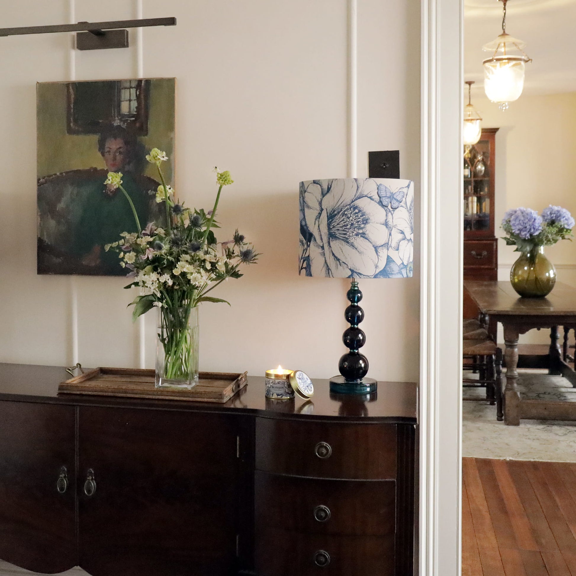 Living room with a wooden sideboard, floral arrangement, and camelia lampshade.