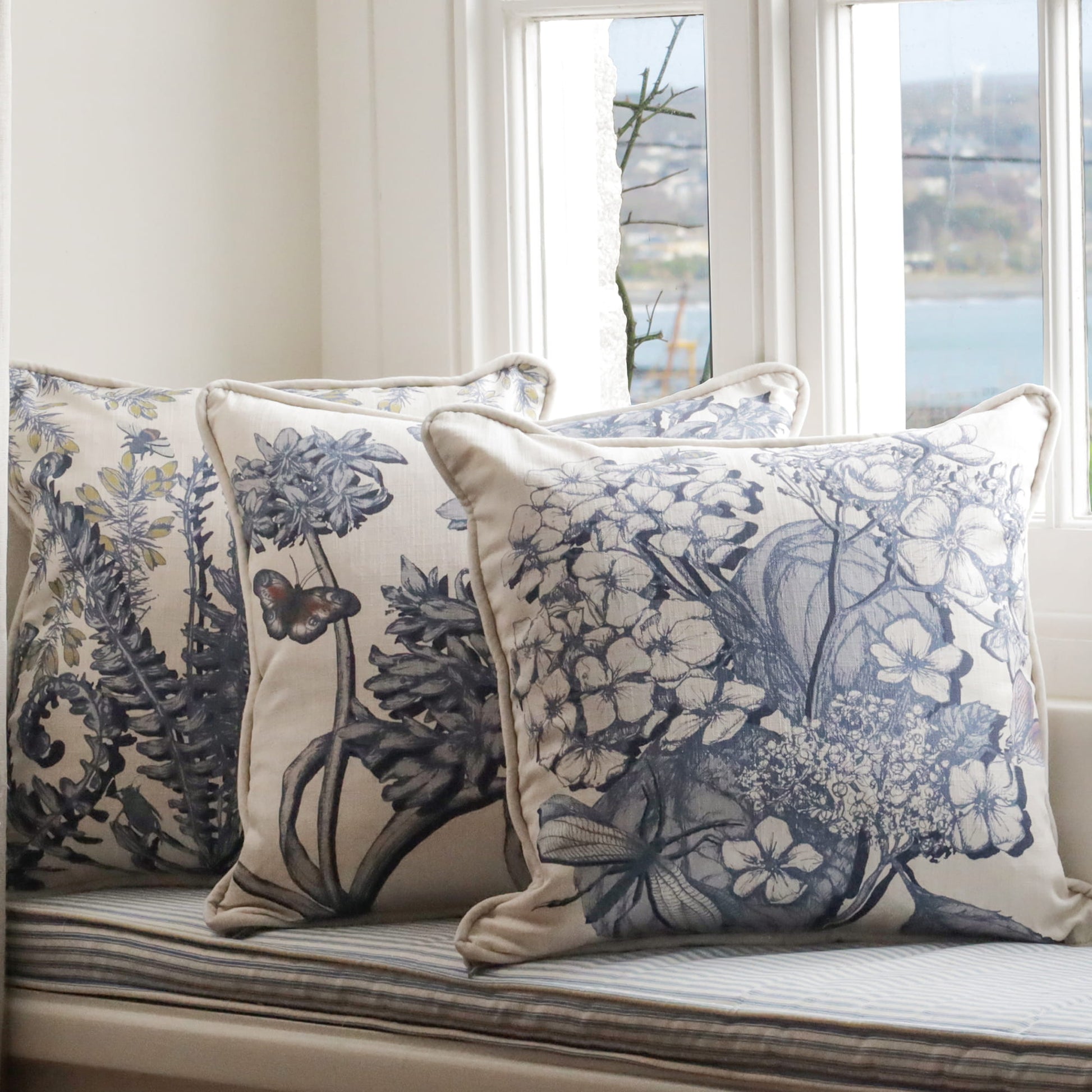 Decorative pillows with hydrangea, agapanthus & fern floral patterns on a window seat.