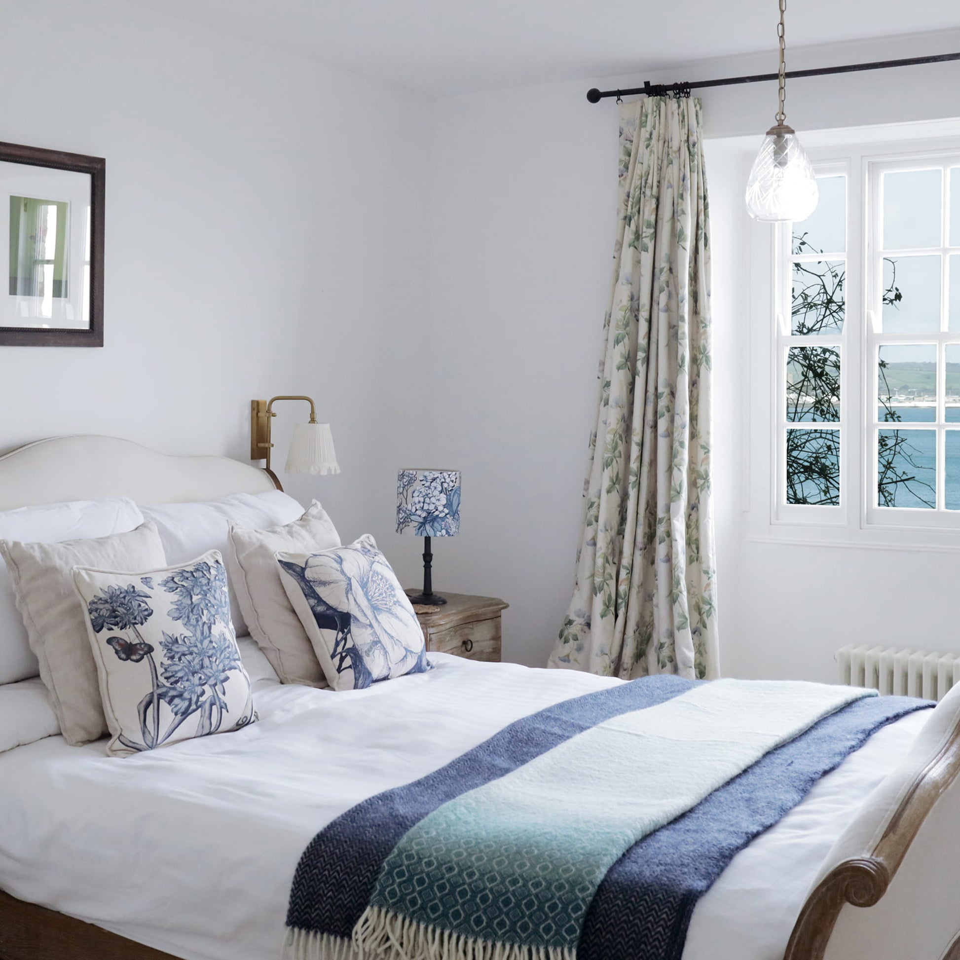 Cozy bedroom with a bed, agapanthus and camelia pillows, and a window with curtains.