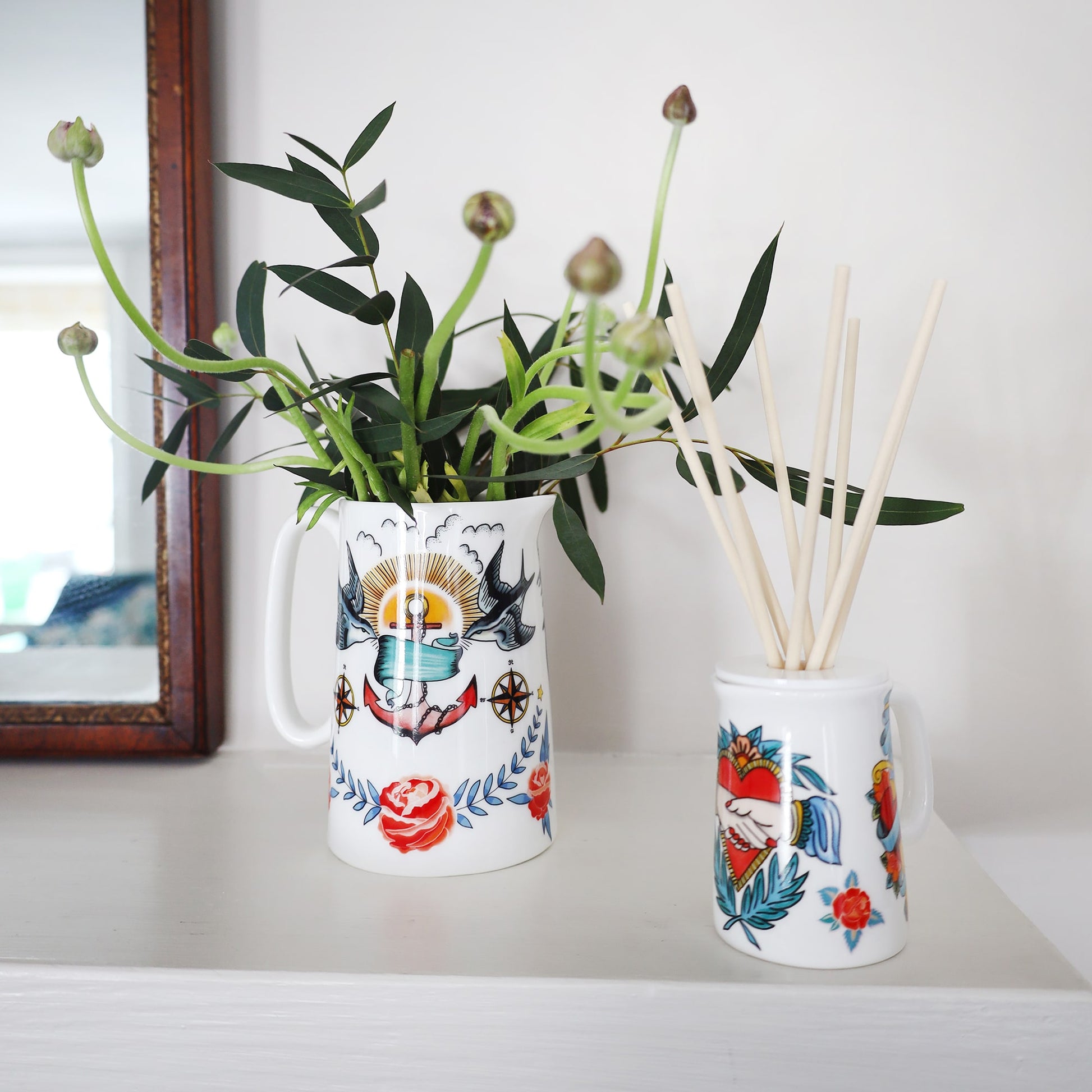 Sailors Story room diffuser with natural reeds on a shelf with another Cream Jug with flowers in,you can see the mirrors reflection.