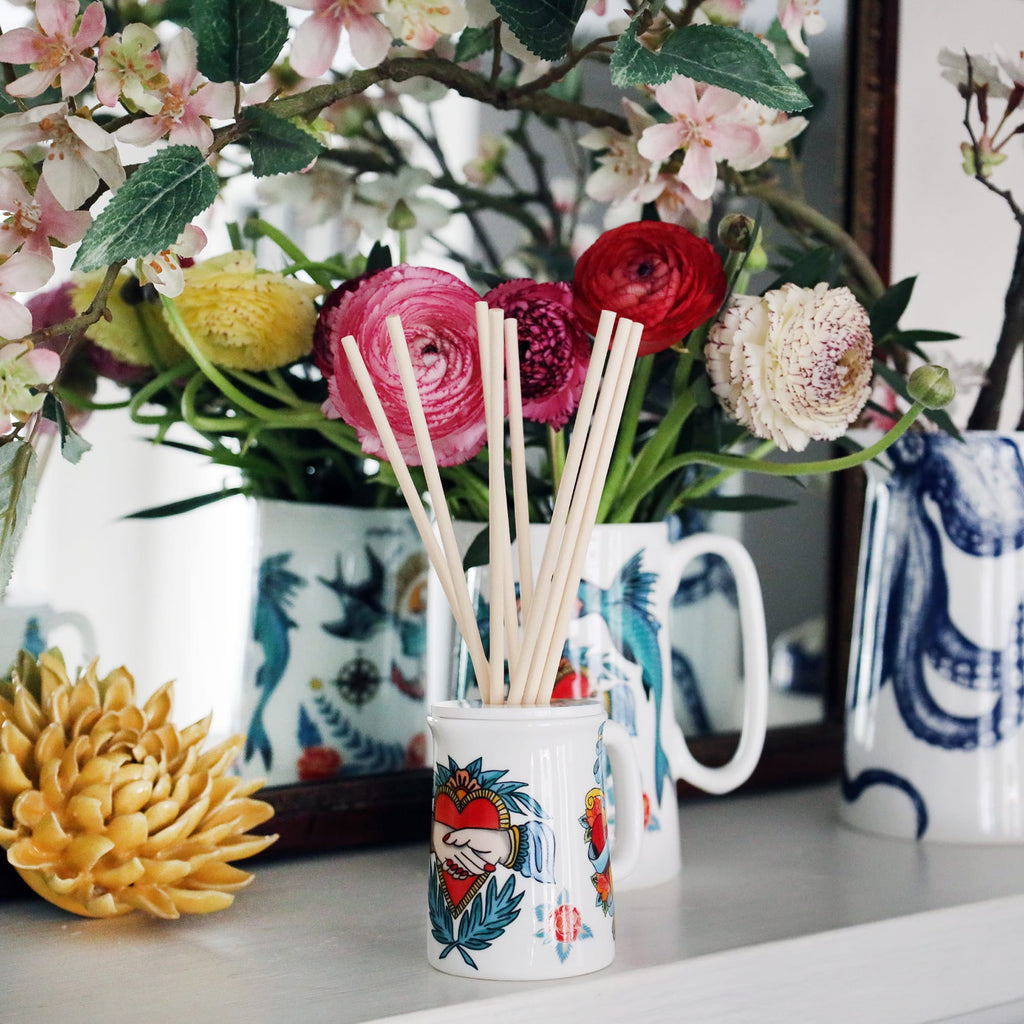 Sailors Story room diffuser with natural reeds on a shelf with other Cream Jugs,you can see the mirrors reflection.
There is also a vase of flowers and a ceramic flower propped against the mirror.