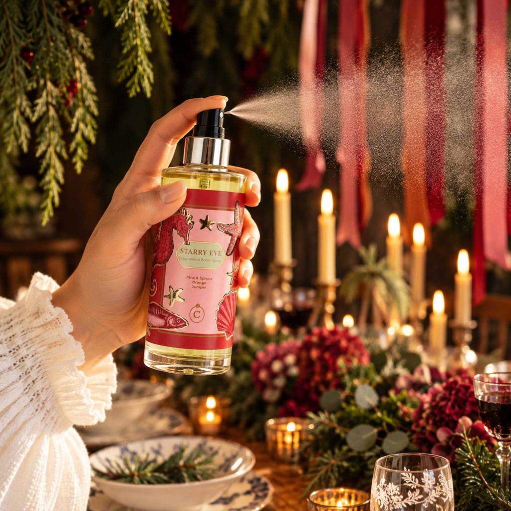 Cream Cornwall Starry Eve room spray being misted over a festive Christmas table, surrounded by candlelight, greenery and rich red seasonal details.