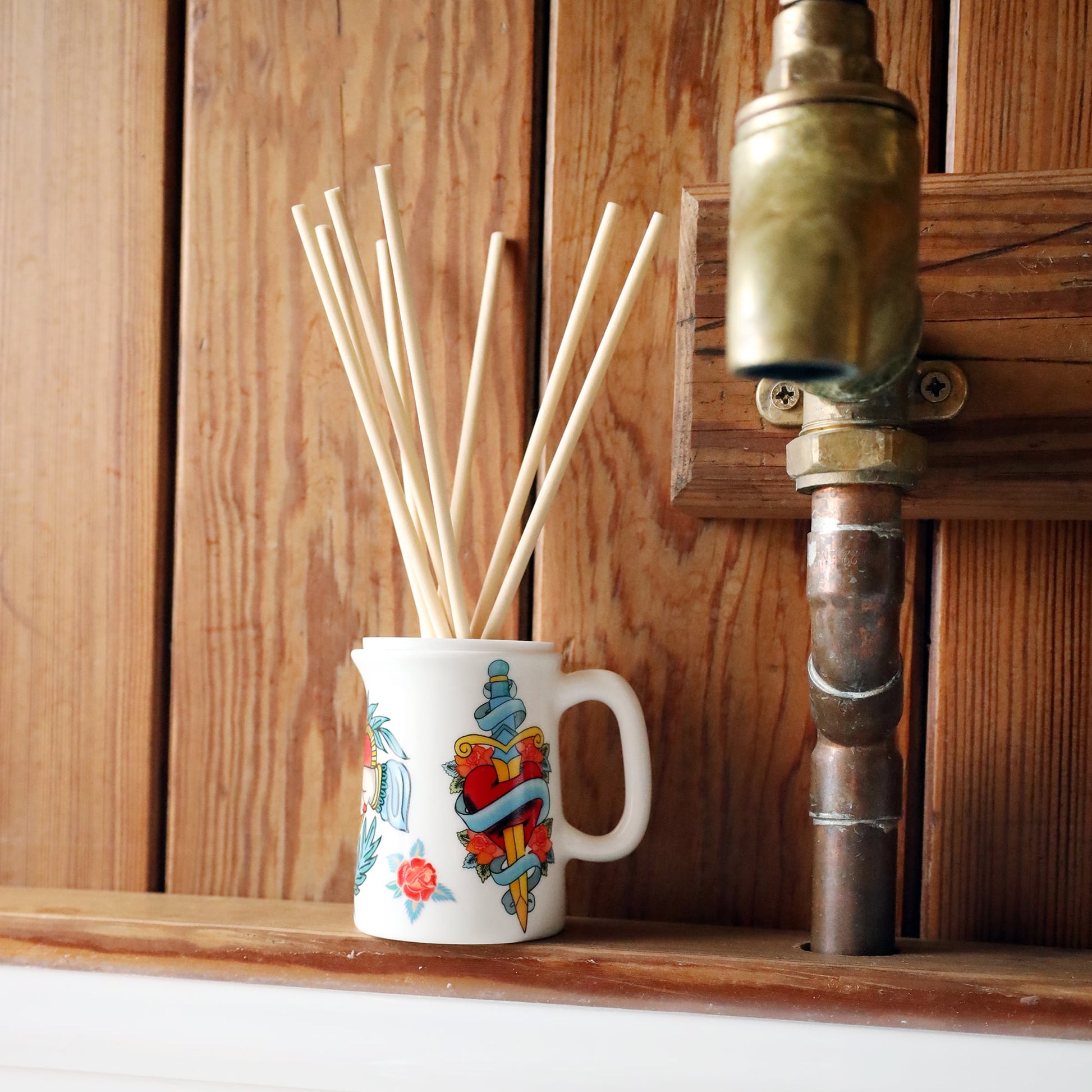 Sailors Story room diffuser with natural reeds on a wooden shelf next to a copper tap in front of wood T & G