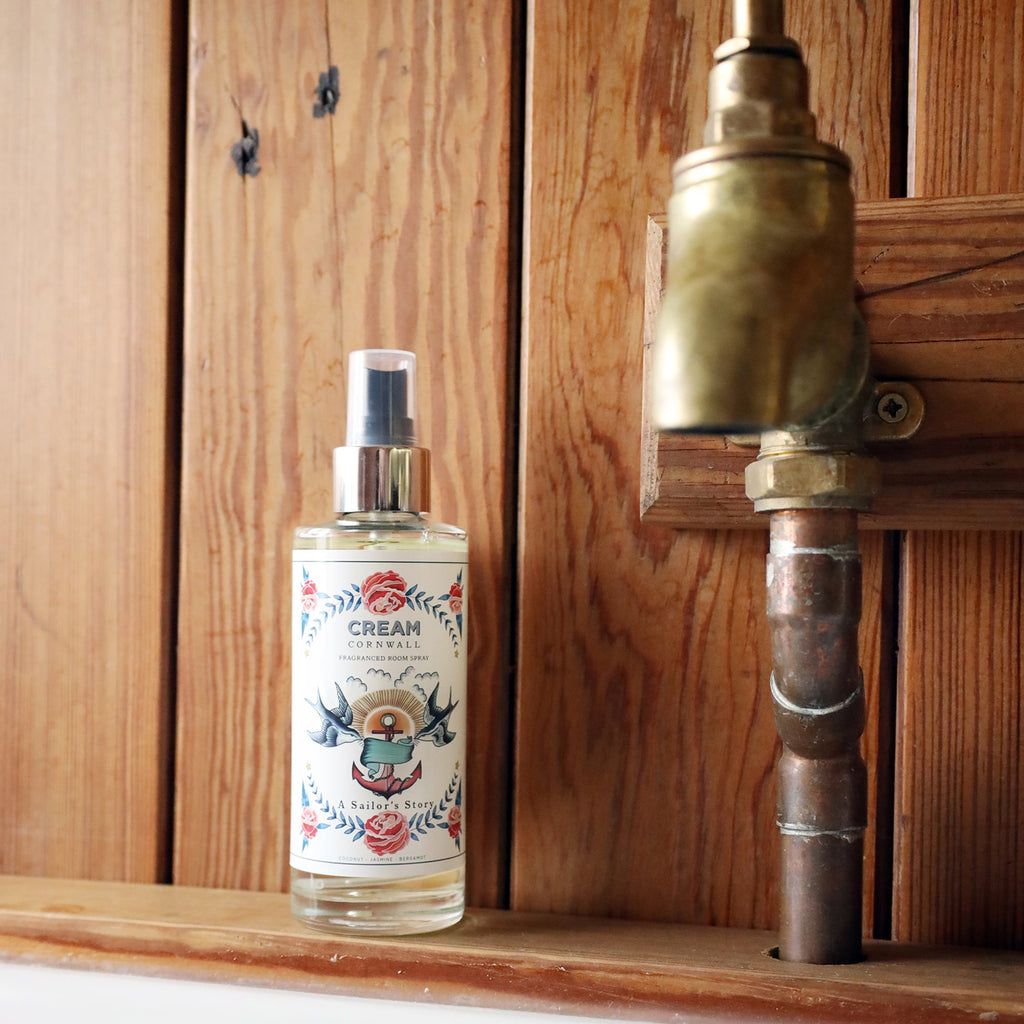 Fragrance Room Spray glass bottle with atomiser top,placed on a wooden shelf next to a copper tap on a wood T & G wall.