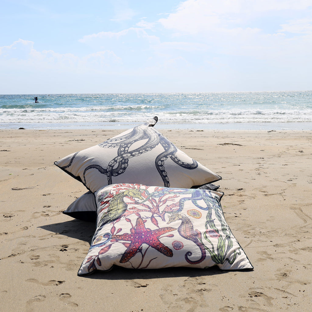 Two decorative pillows with ocean-themed designs on a sandy beach.