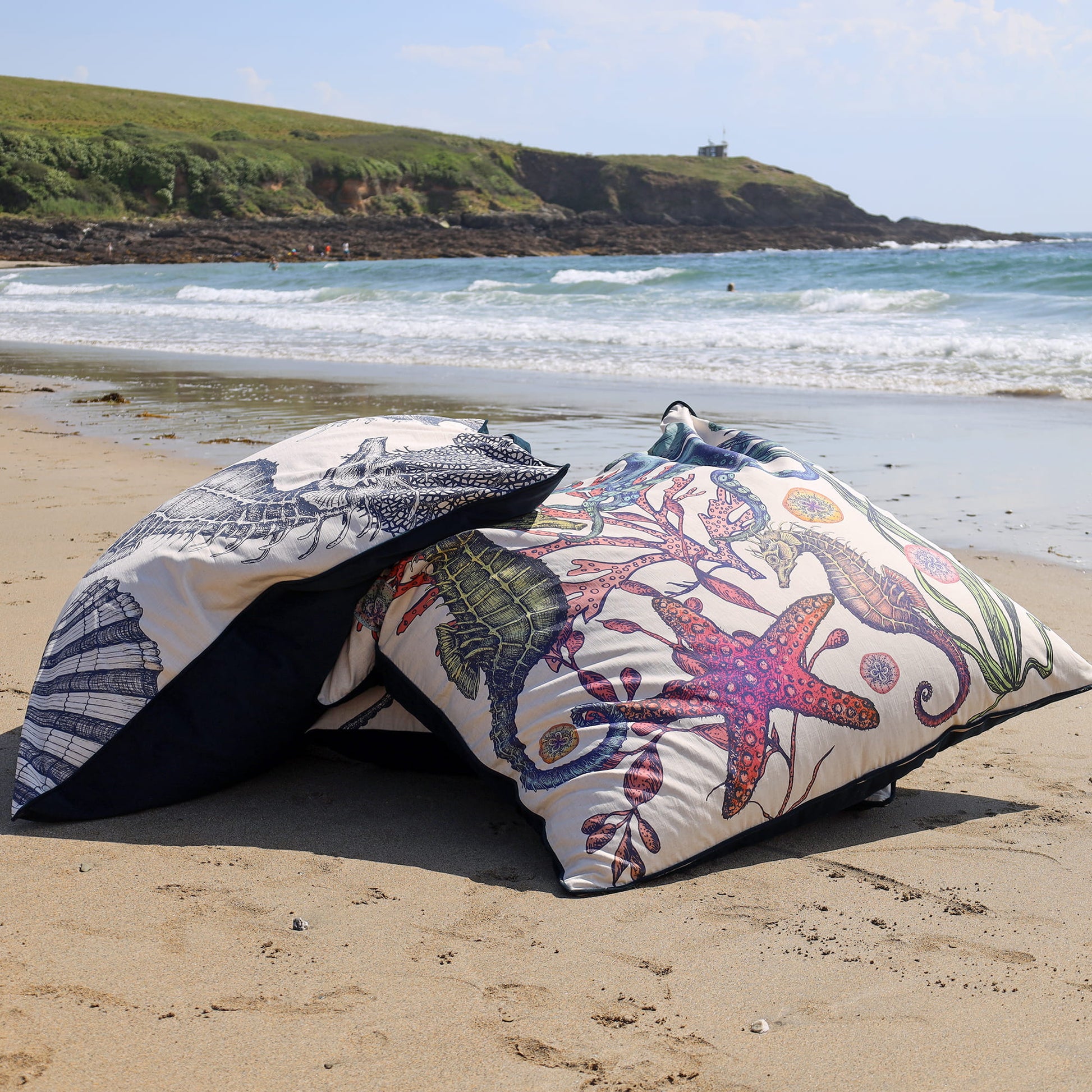 Two bean bags with floral and shell patterns on a sandy beach.