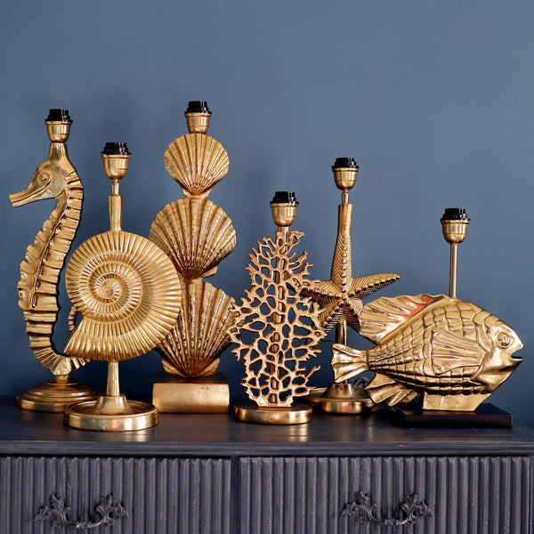 ChatGPT said:

A collection of gold coastal-inspired lamp bases, including designs shaped like a seahorse, ammonite, scallop shells, coral, starfish, and fish, displayed together on a dark cabinet against a blue wall.