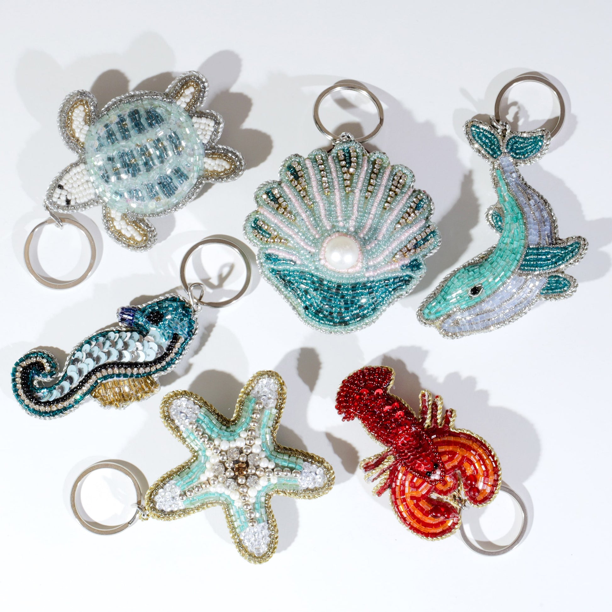 Collection of decorative keychains shaped like a turtle, shell, dolphin, mustache, starfish, and lobster on a white background.