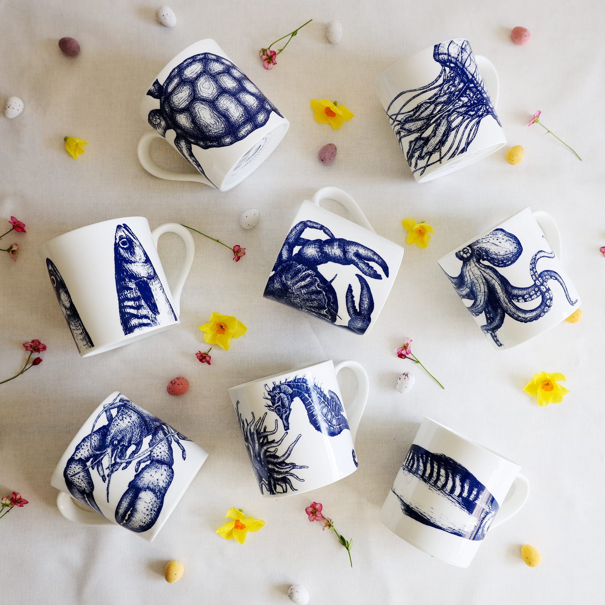 Set of white mugs with blue sea creature illustrations on a light background with flowers.