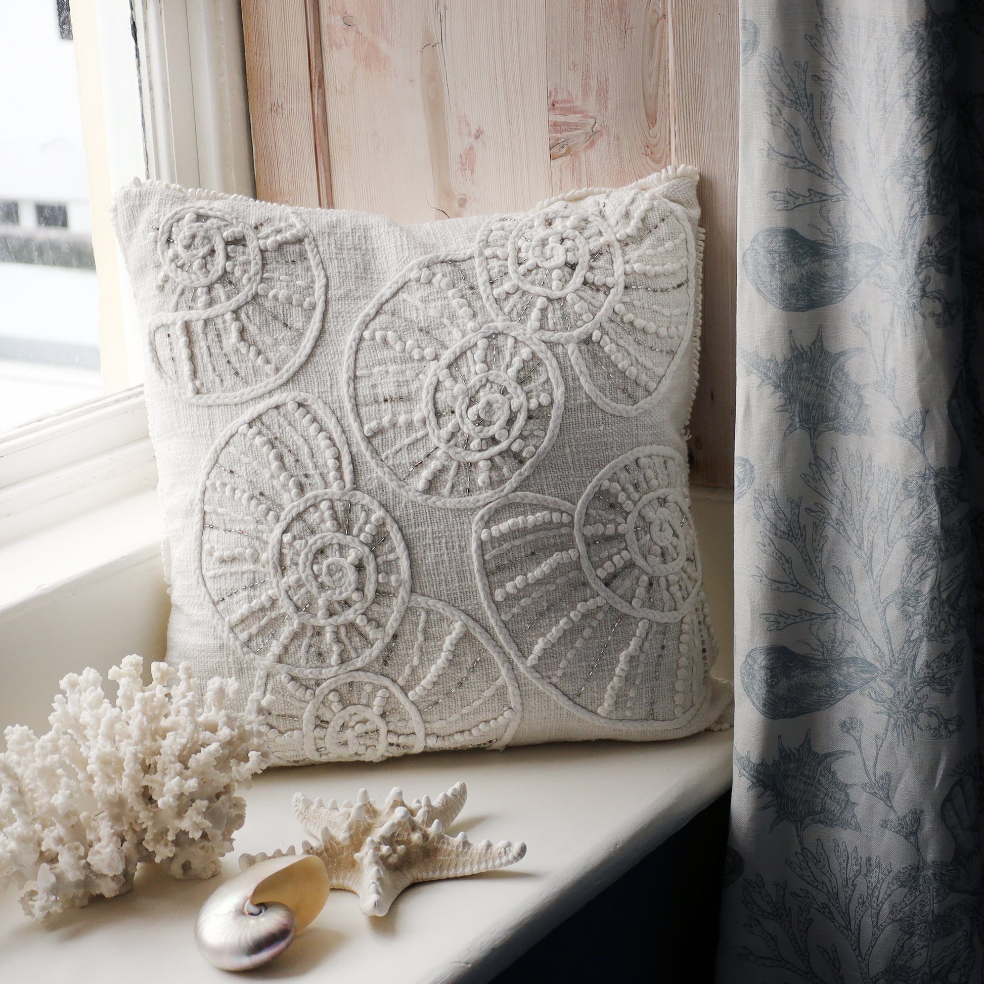 Decorative pillow with lace-like pattern on a windowsill with corals and shells.