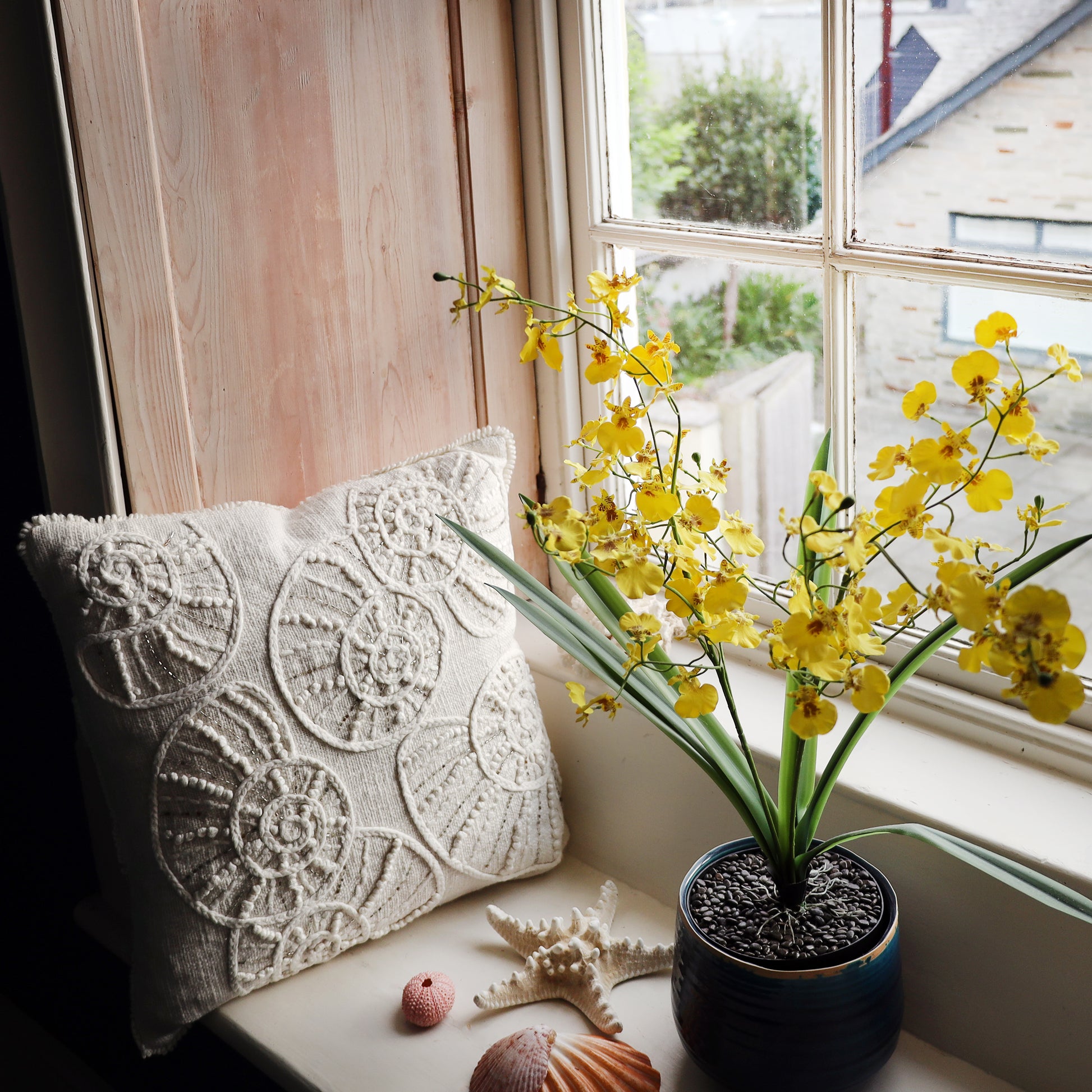 Decorative pillow and potted yellow orchids on a windowsill with a view of a house.